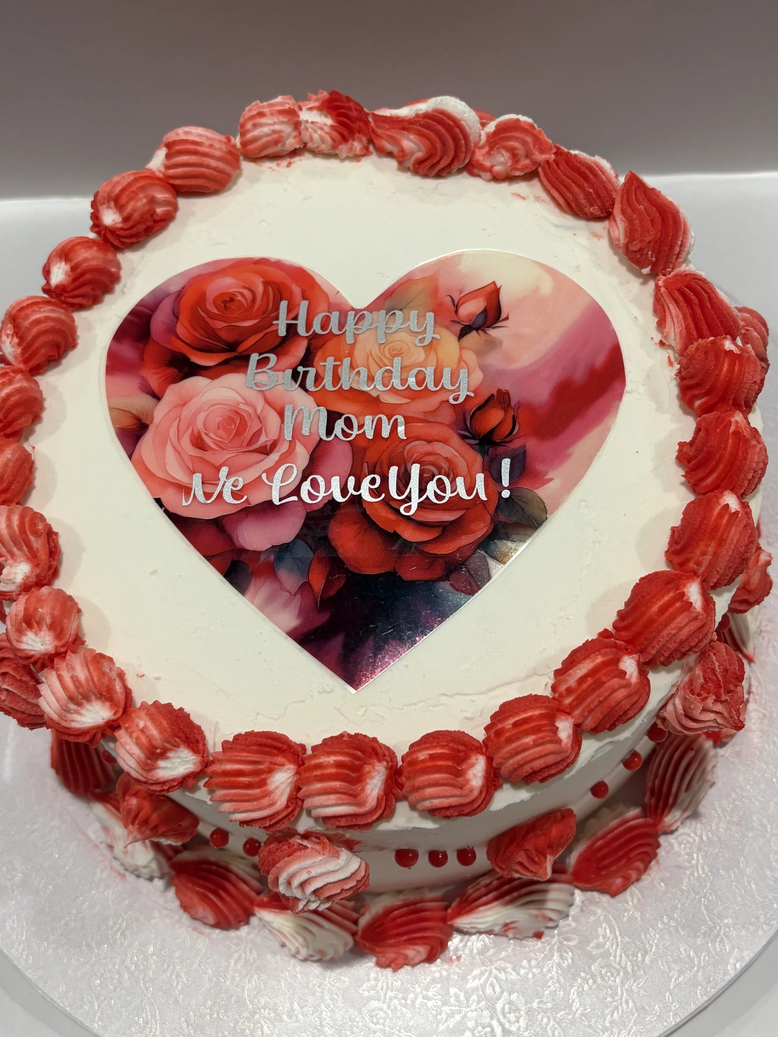 A round white cake with a red rose border and a heart-shaped photo insert with "Happy Birthday" lettering.