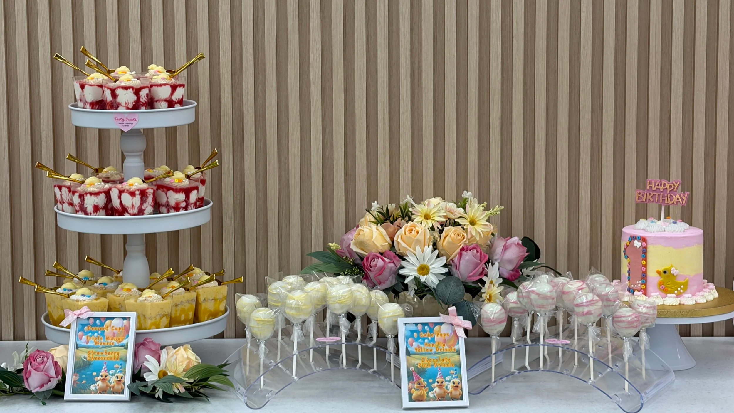 Full dessert bar display with tiered stands of cake pops and cupcakes, a small cake, and floral arrangements.