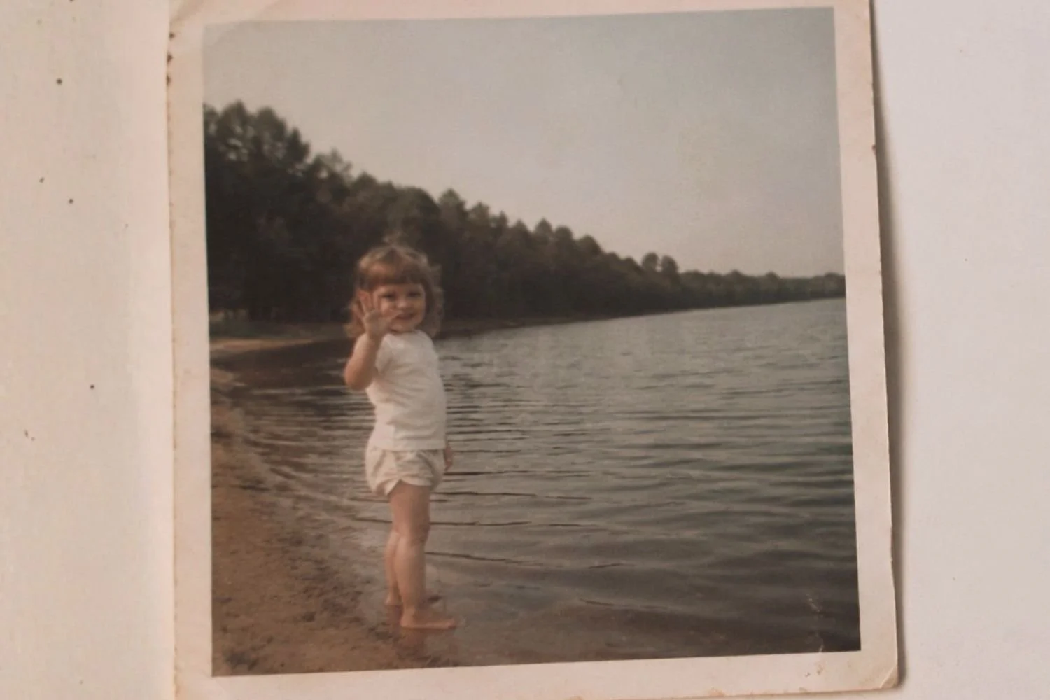 A nostalgic childhood photo of a young girl waving on a beach, representing how early childhood scarcity shapes adult money psychology.