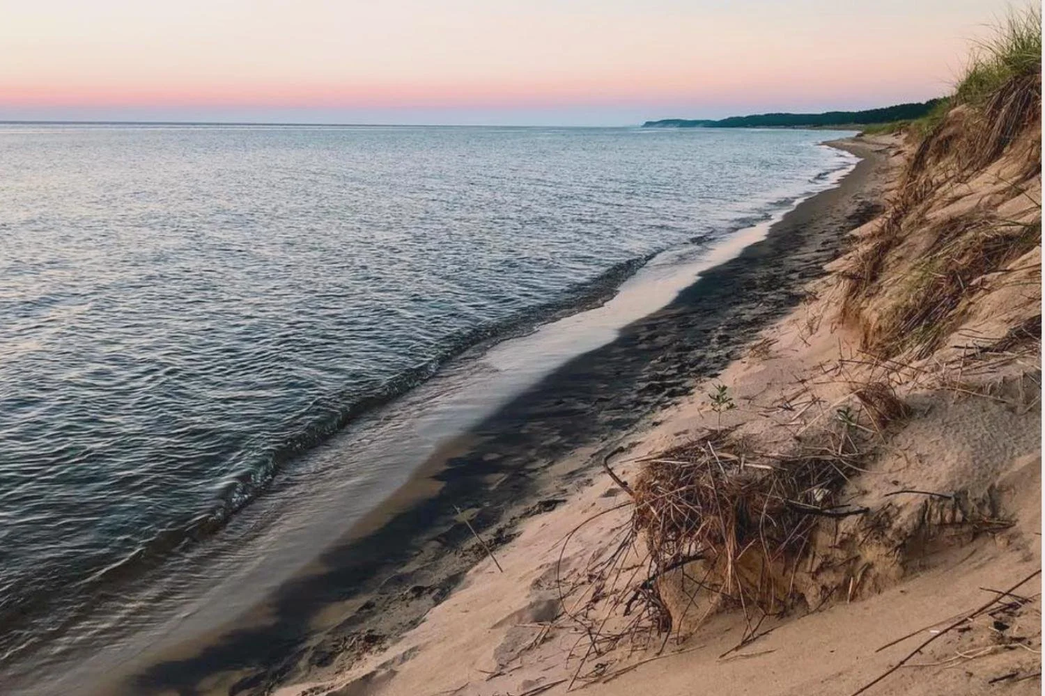 Scenic view of a sandy beach and grassy dunes along the blue waters of Lake Michigan at dusk.