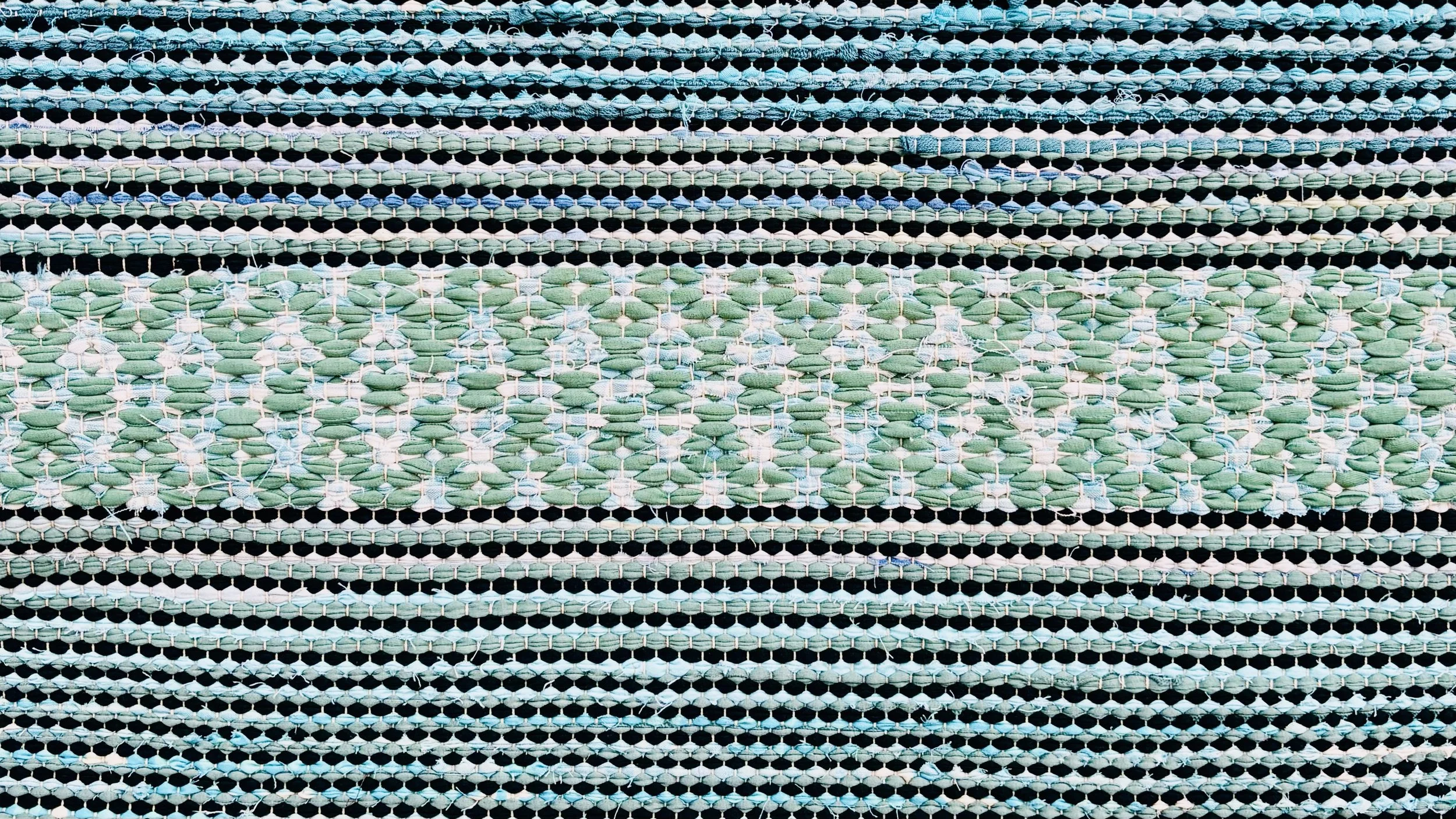 Close-up view of a woven fabric with horizontal stripes in shades of black, white, and green.