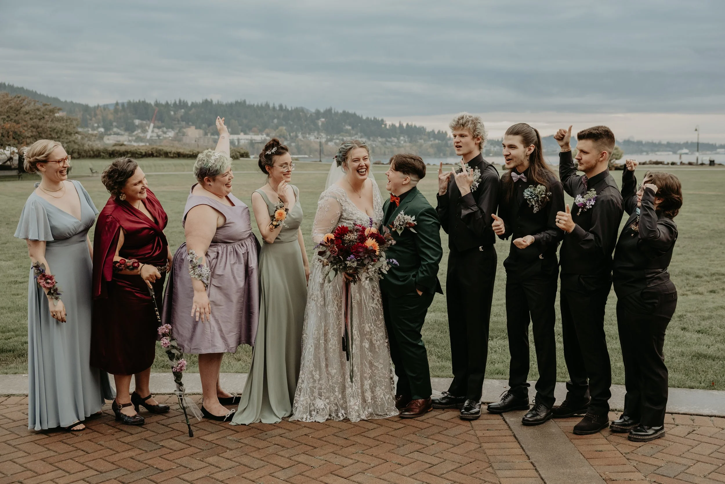 A wedding party outdoors with a bride, groom, bridesmaids, and groomsmen smiling and celebrating.