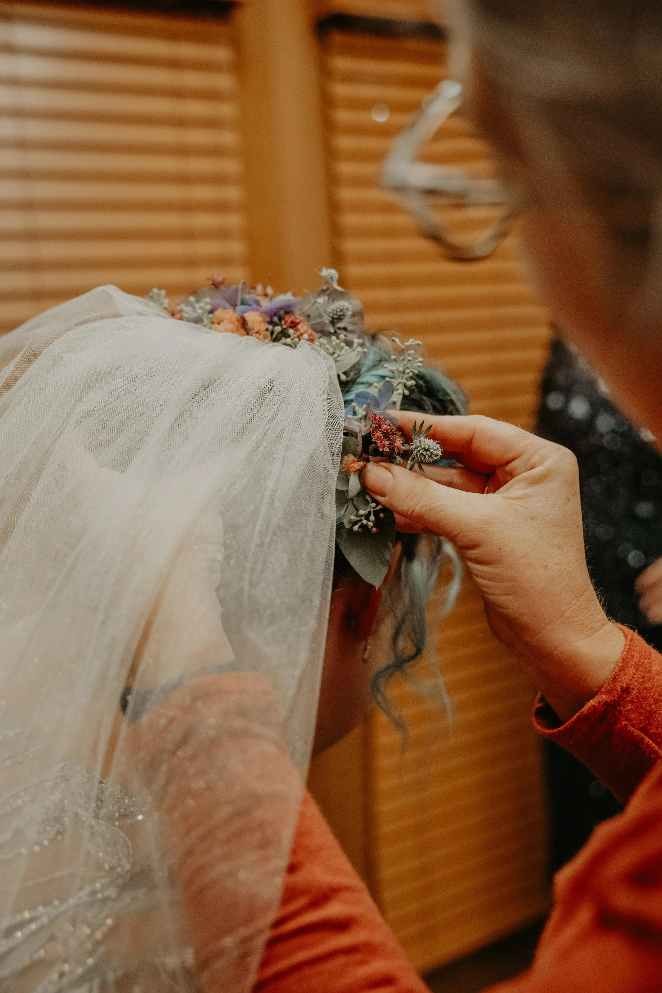 Auntie M placing a wedding floral hair piece with a veil overhead, with wooden blinds in the background.