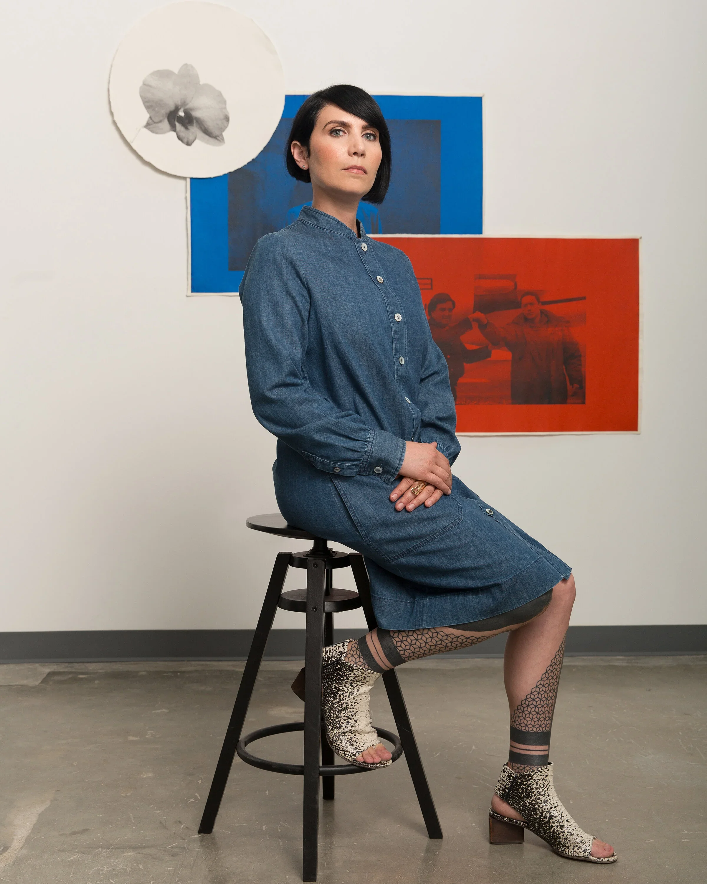 Regina Mamou, sitting on a stool, in a gallery in front of artwork