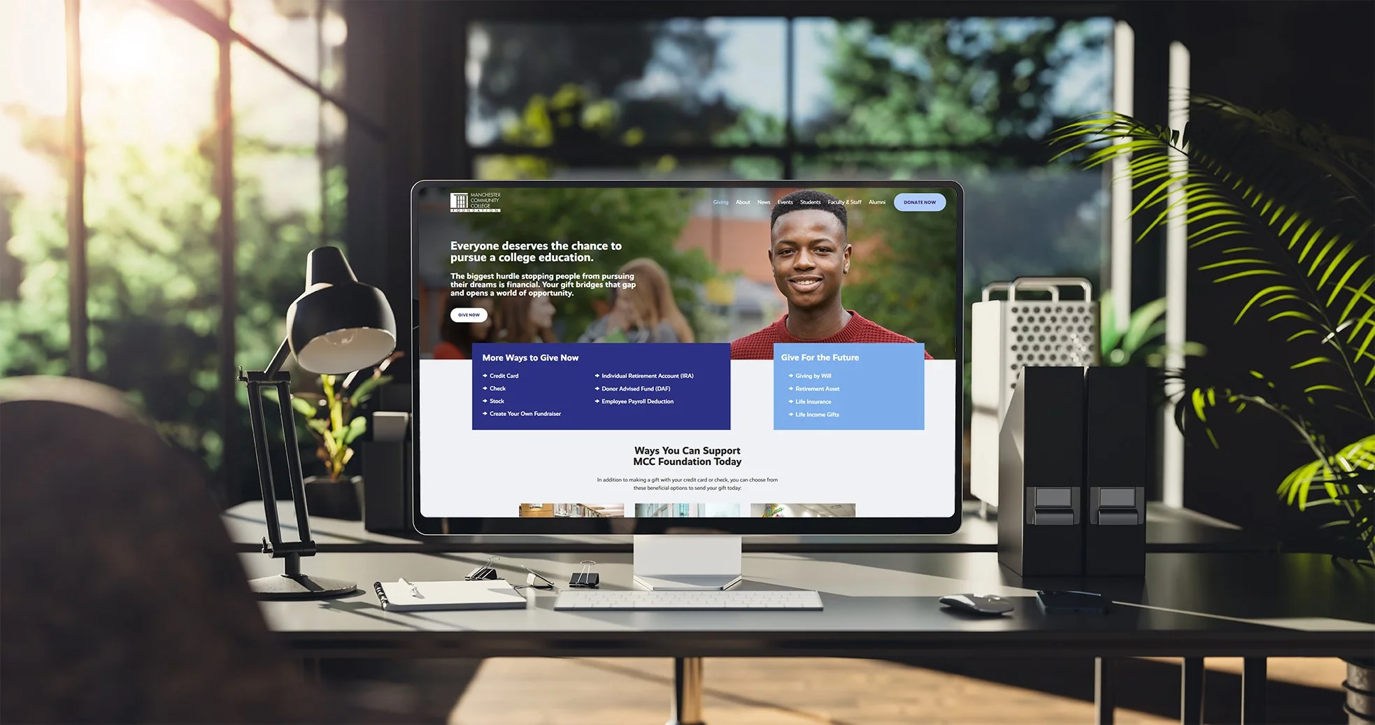 Desktop screen open on MCC Foundation homepage on a clean desk with large windows in the background.