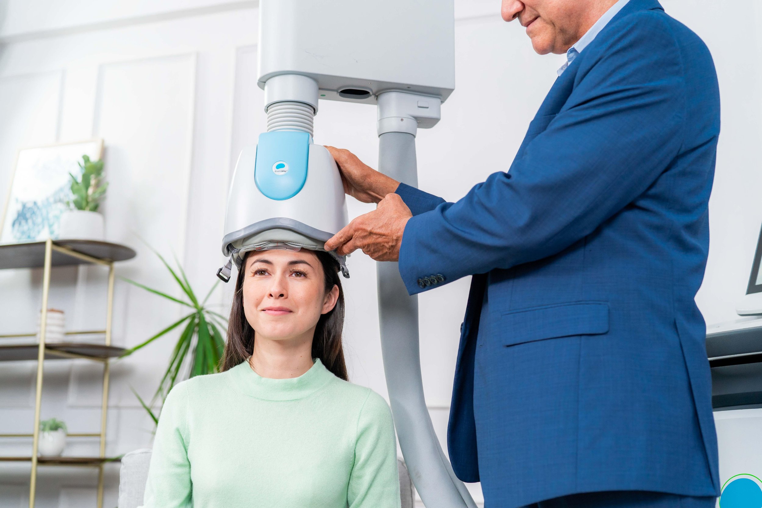 A medical professional in a blue suit adjusts a brain activity monitoring device on a woman's head during a medical examination in a clinical setting.