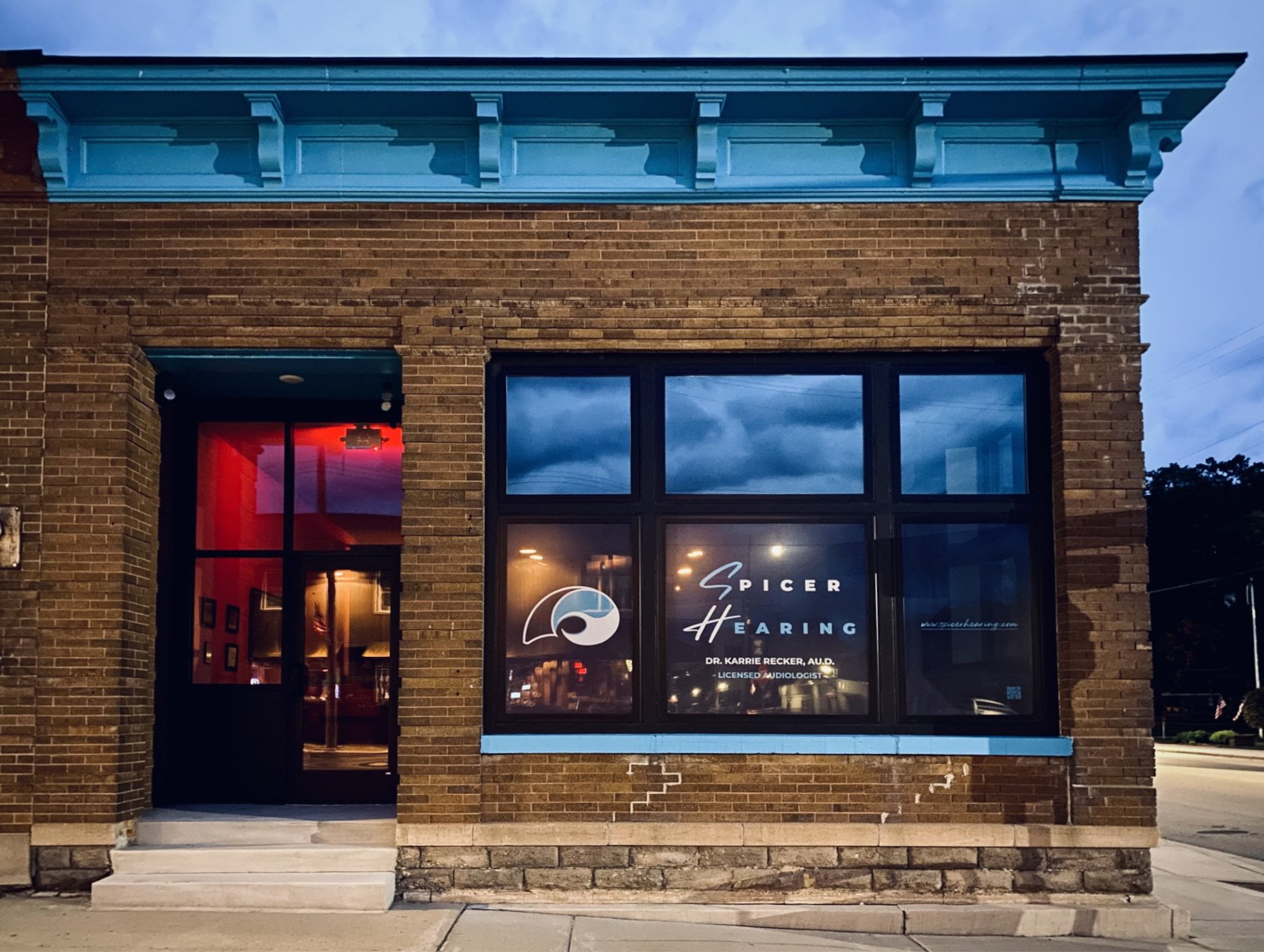 Picture of Spicer Hearing building at night with the windows glowing and a colorful sky in the background.