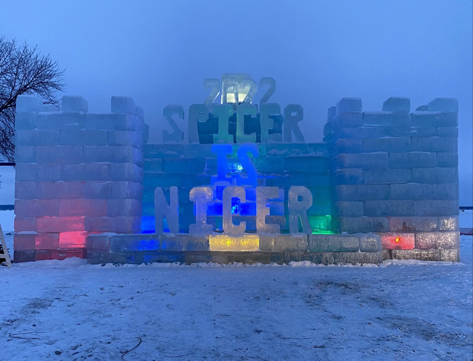 ice castle near evening_lit up with colorful lights_carved in ice is the message, "2022 Spicer is Nicer"