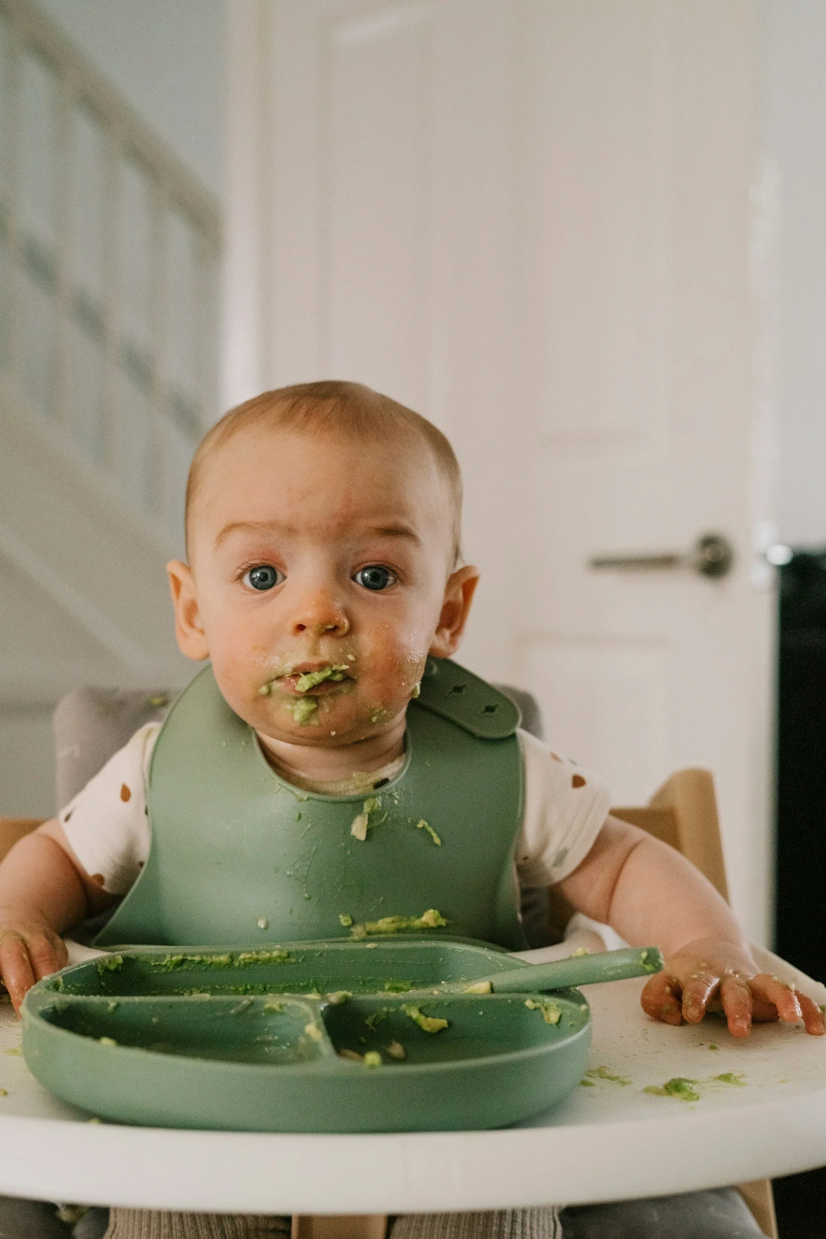 Baby sitting in a high chair eating avocado as a first food