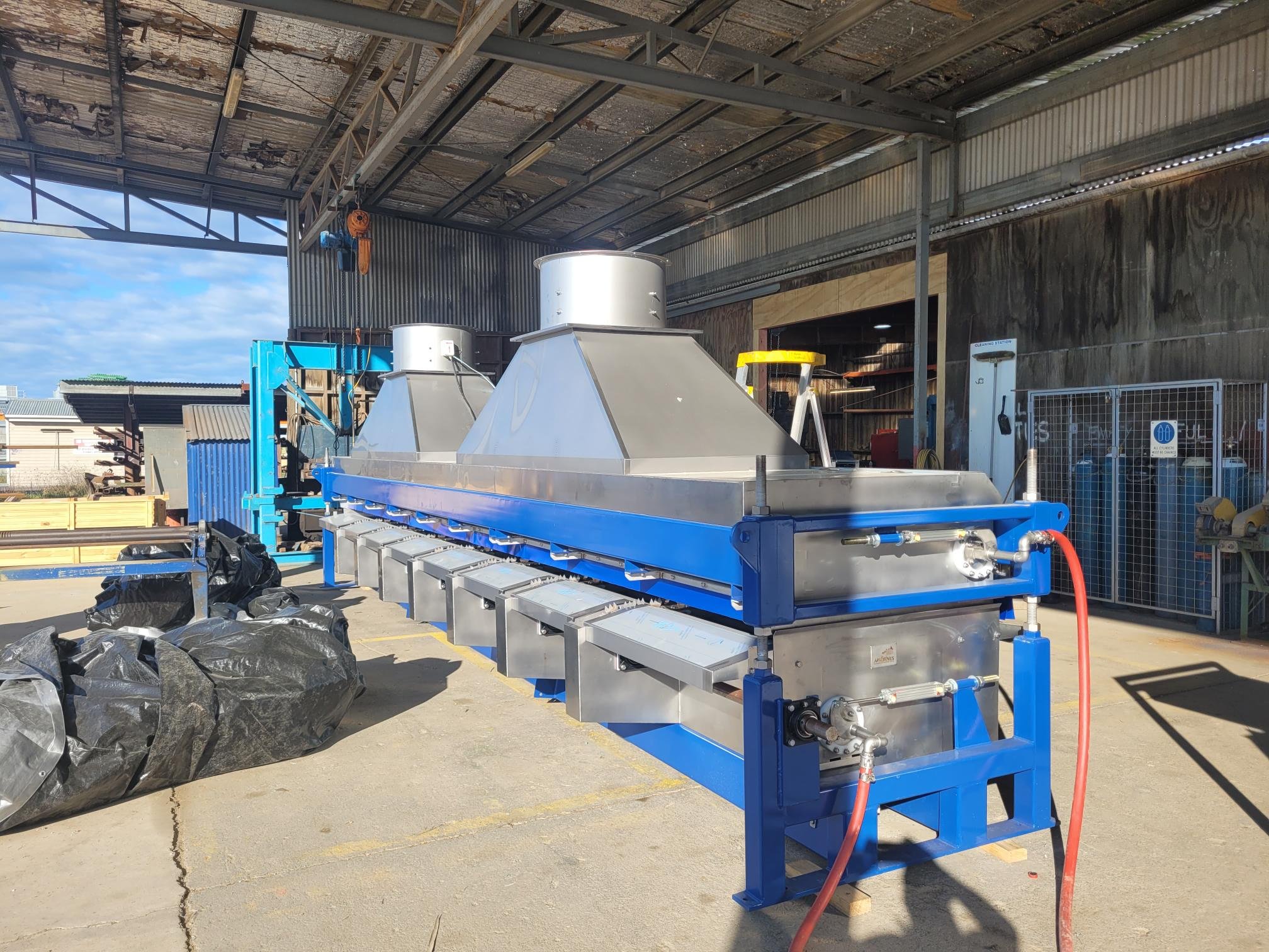 Industrial machinery in a warehouse setting with metal components and blue framework, used for manufacturing or processing purposes.