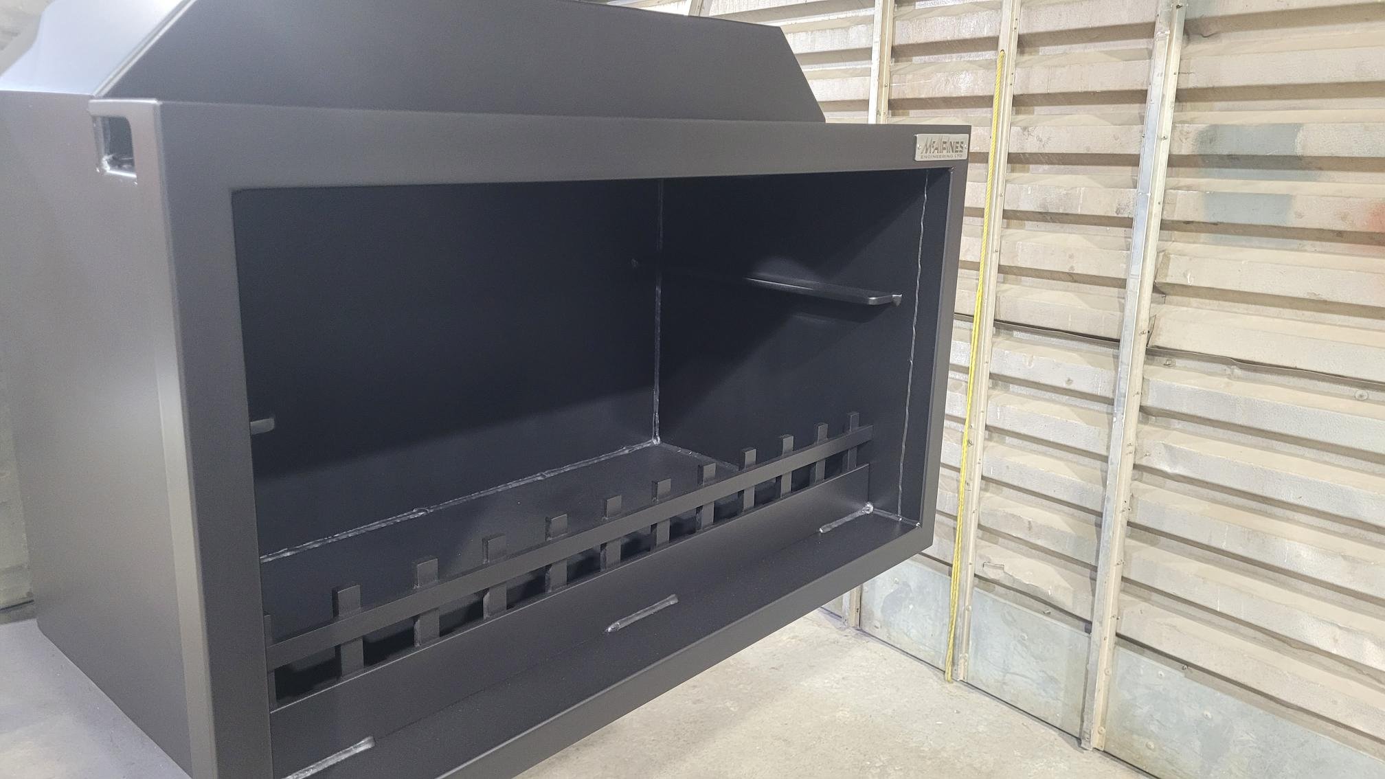 Large metal outdoor fireplace or grill in industrial setting.