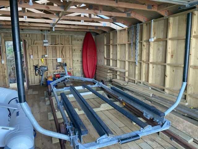 Interior of a wooden garage with a boat trailer and a red kayak.