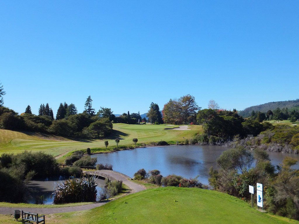 Golf course with a water hazard, trees, and clear blue sky