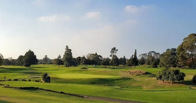 Golf course with green fairways, trees, and a clear sky.