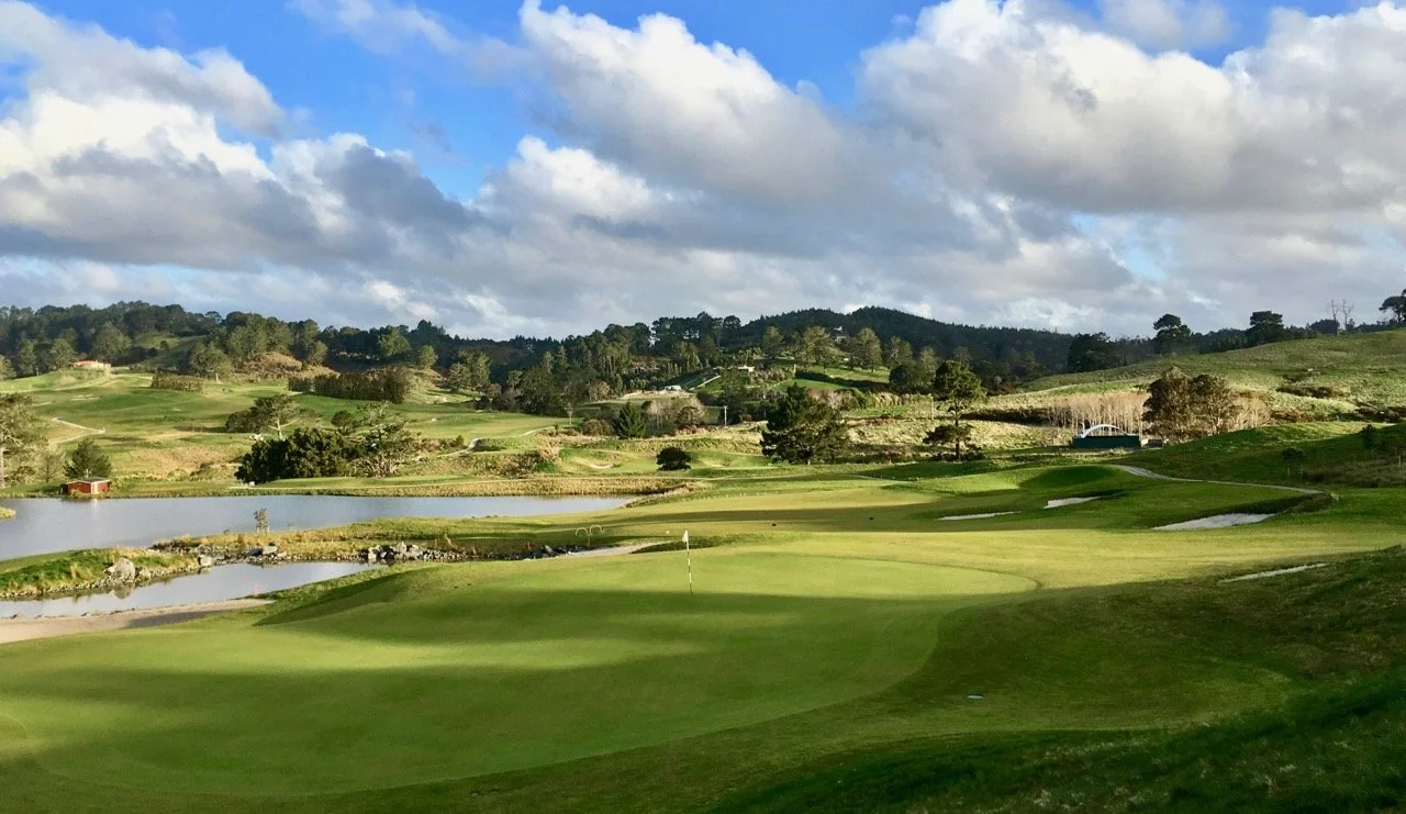 Scenic golf course landscape with rolling hills and a pond under a cloudy sky.