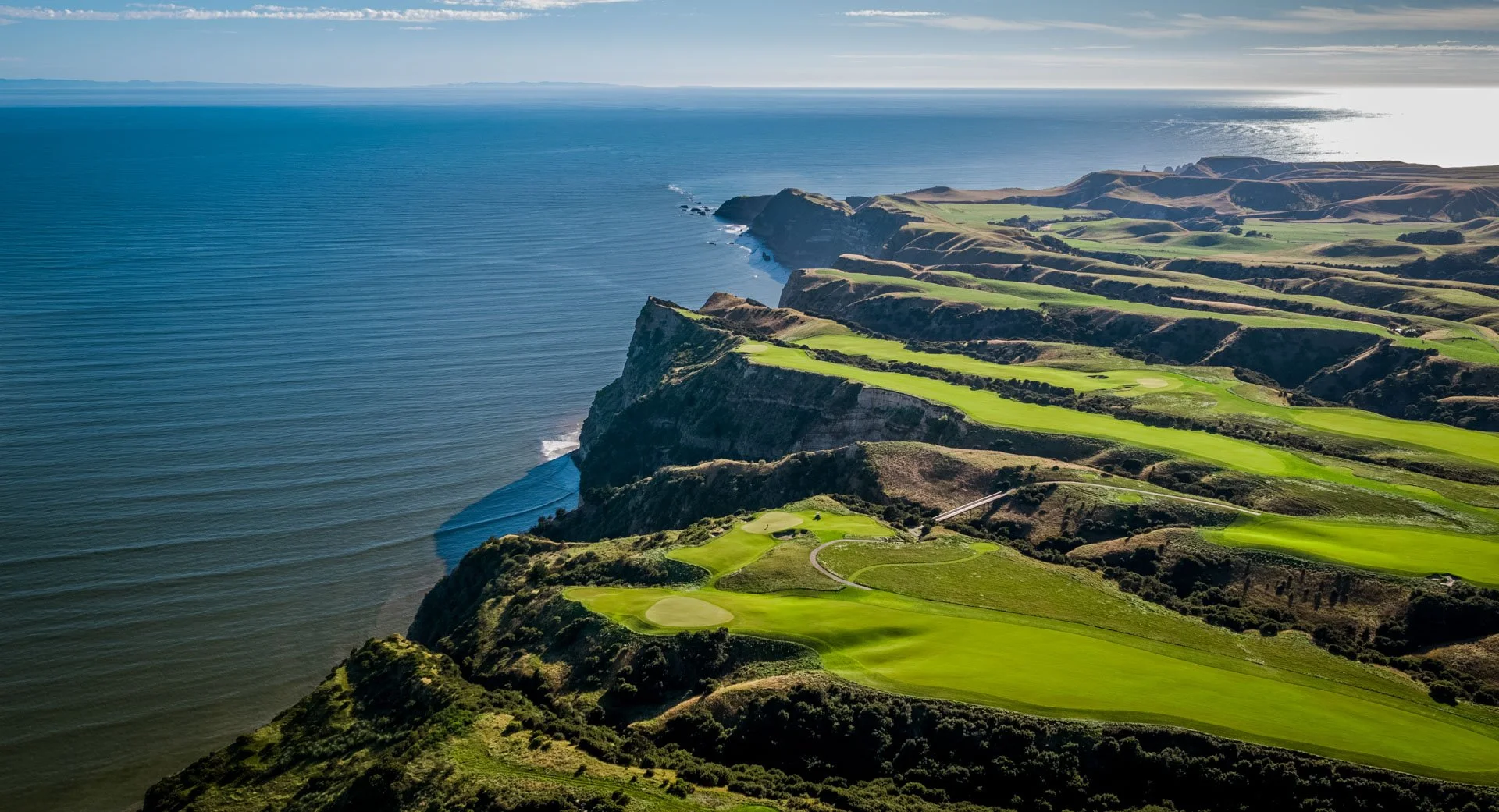 Aerial view of a golf course on coastal cliffs with ocean in the background.
