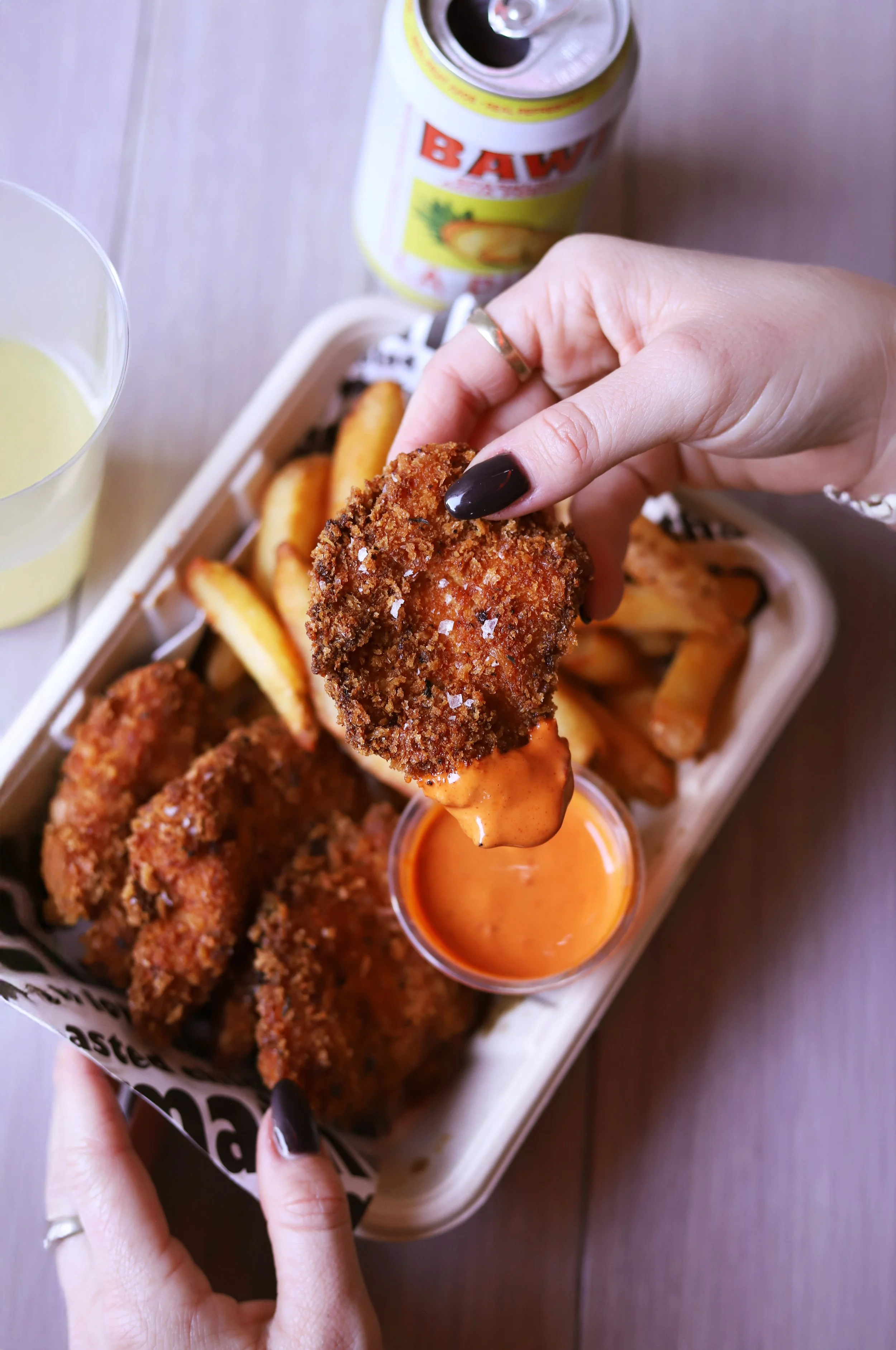 Crispy Dirty Chicken Tenders dipped in Spicy Pepper sauce. With a side of fries and a crisp cold agua freya drink in the background
