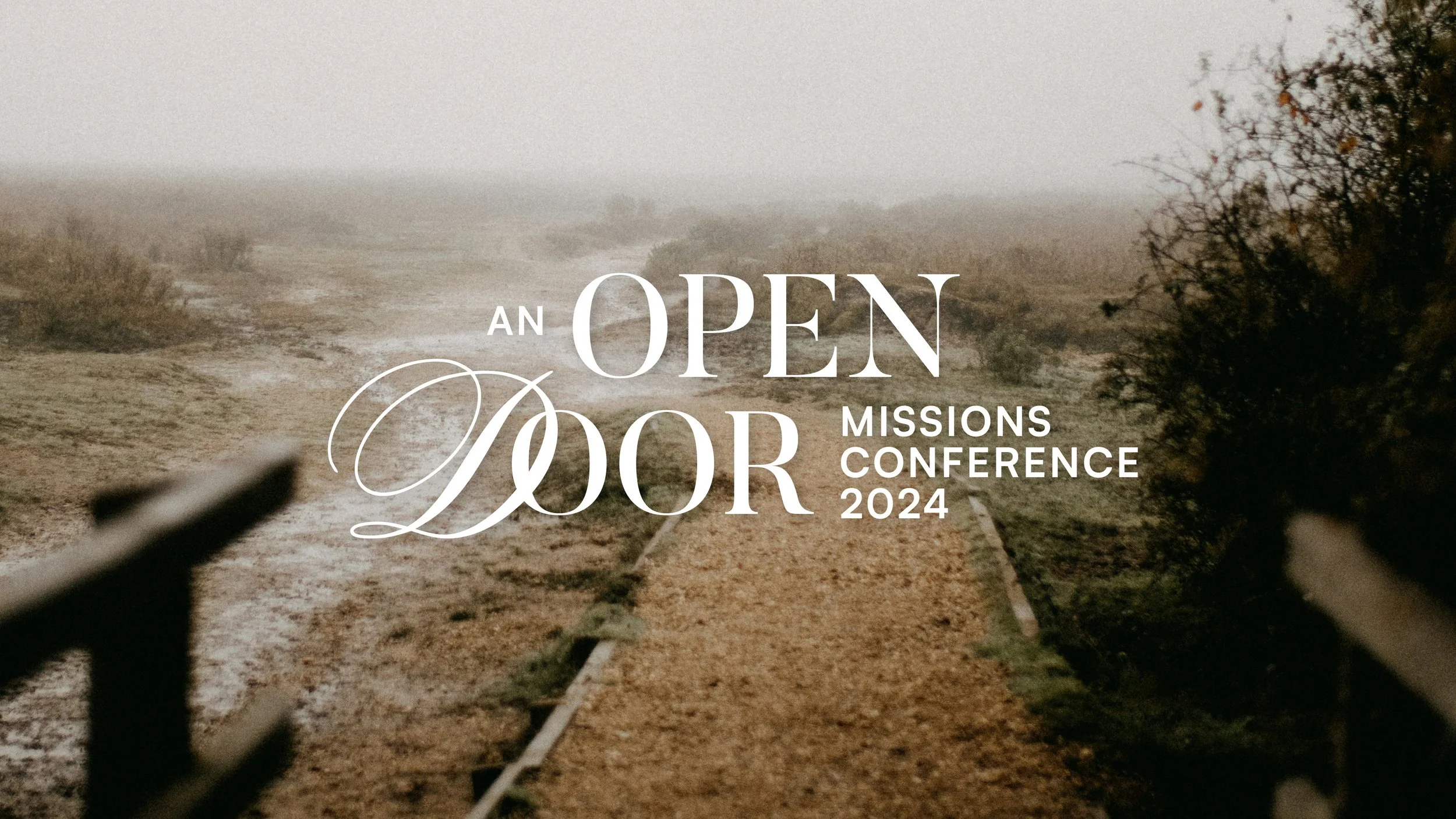 A foggy, deserted dirt road in a rural area with trees and bushes on the sides, overlaid with white text announcing the 'Open Door Missions Conference 2024'.