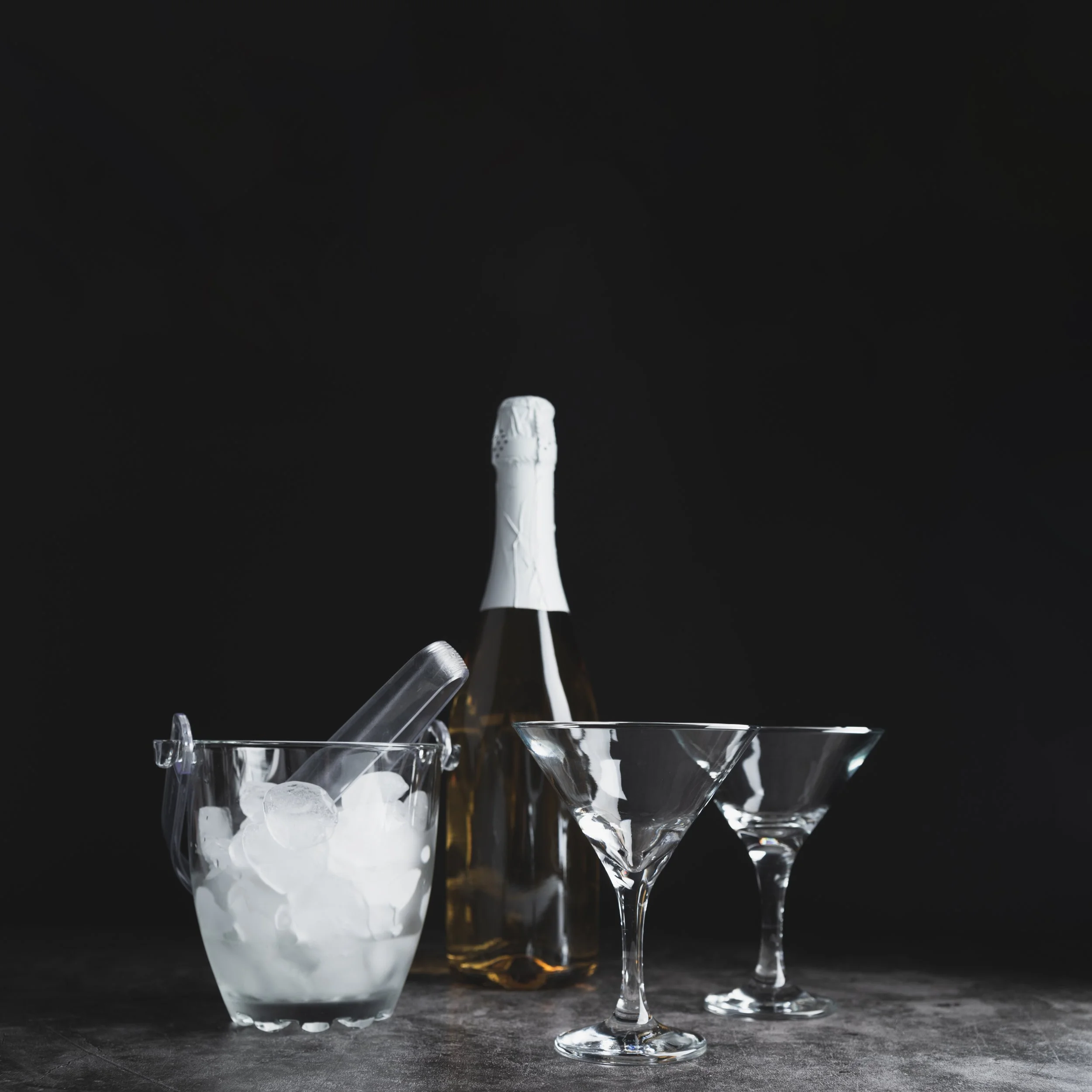 A tall glass filled with ice and a white liquid, possibly milk, with other empty cocktail glasses on a dark surface against a black background.