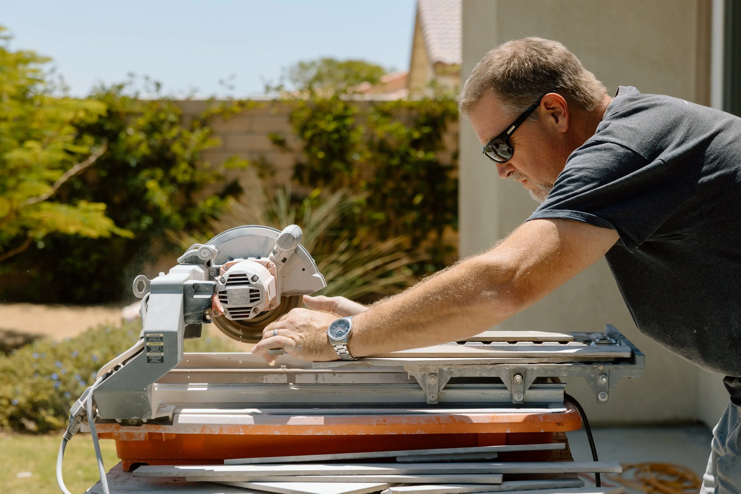 Man cutting tile outside with a miter saw on a work table.