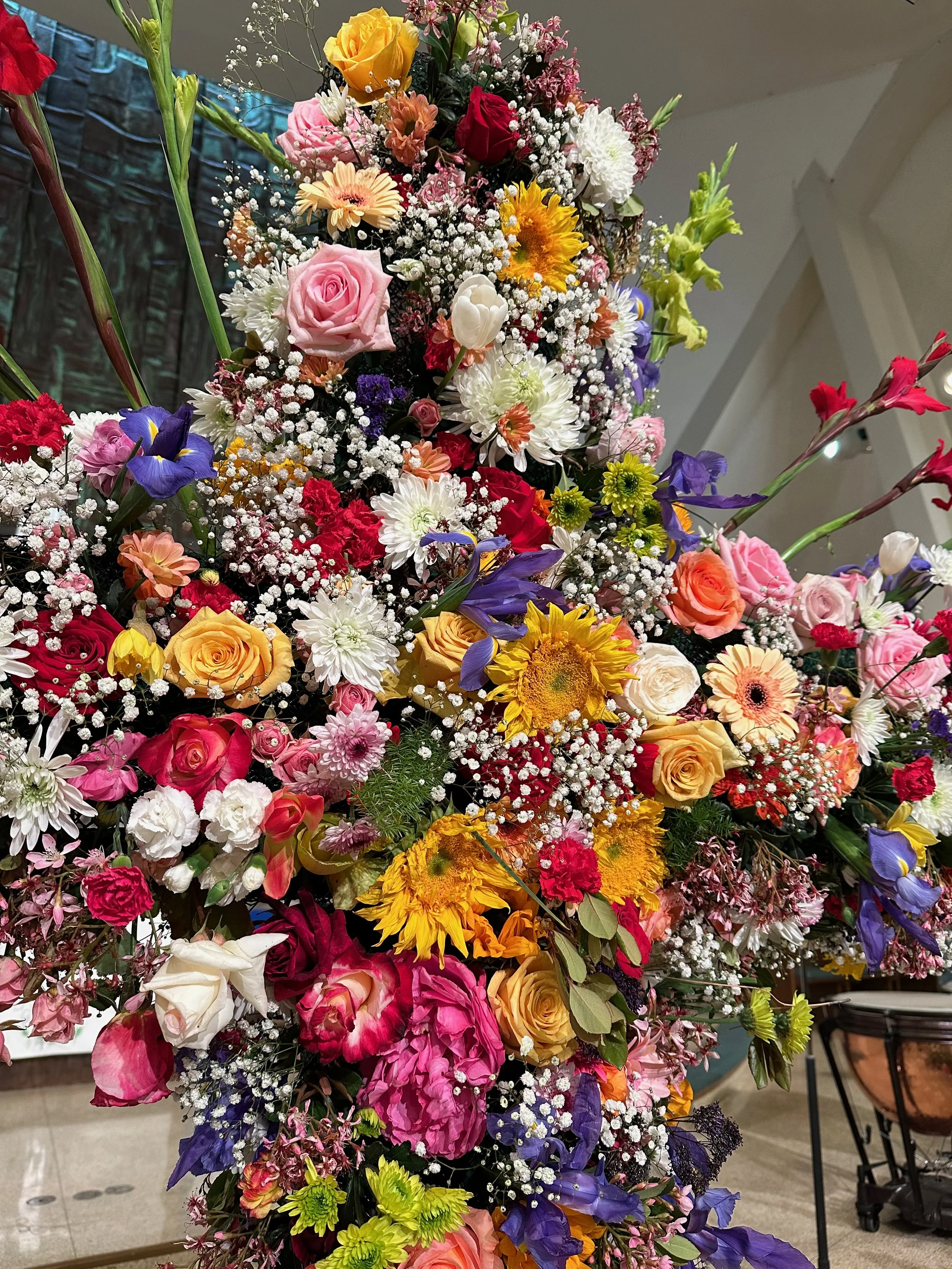 A large, colorful floral arrangement with roses, sunflowers, daisies, irises, and baby's breath.