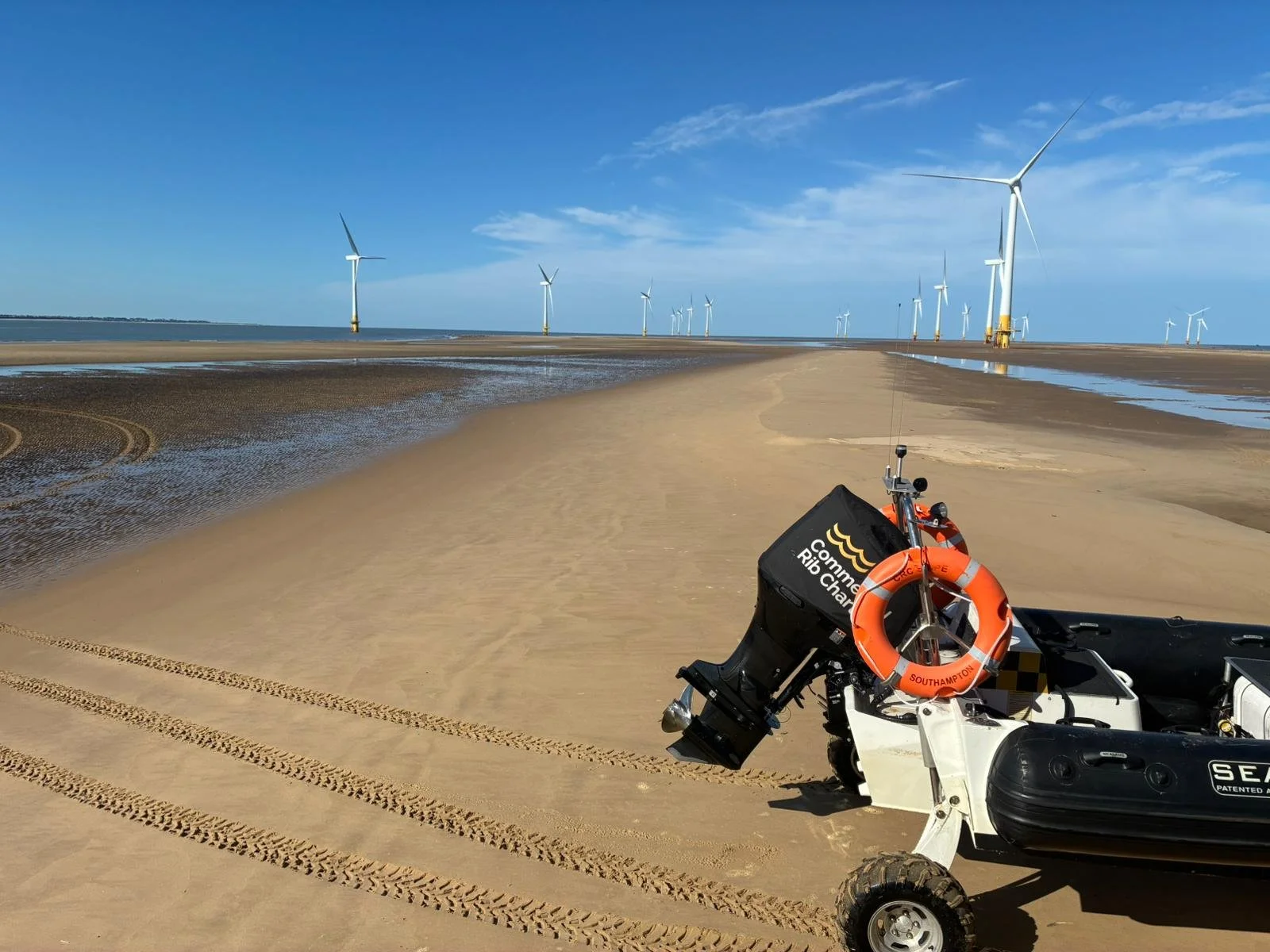 A robot on sand with wind turbines in the background and a clear blue sky.