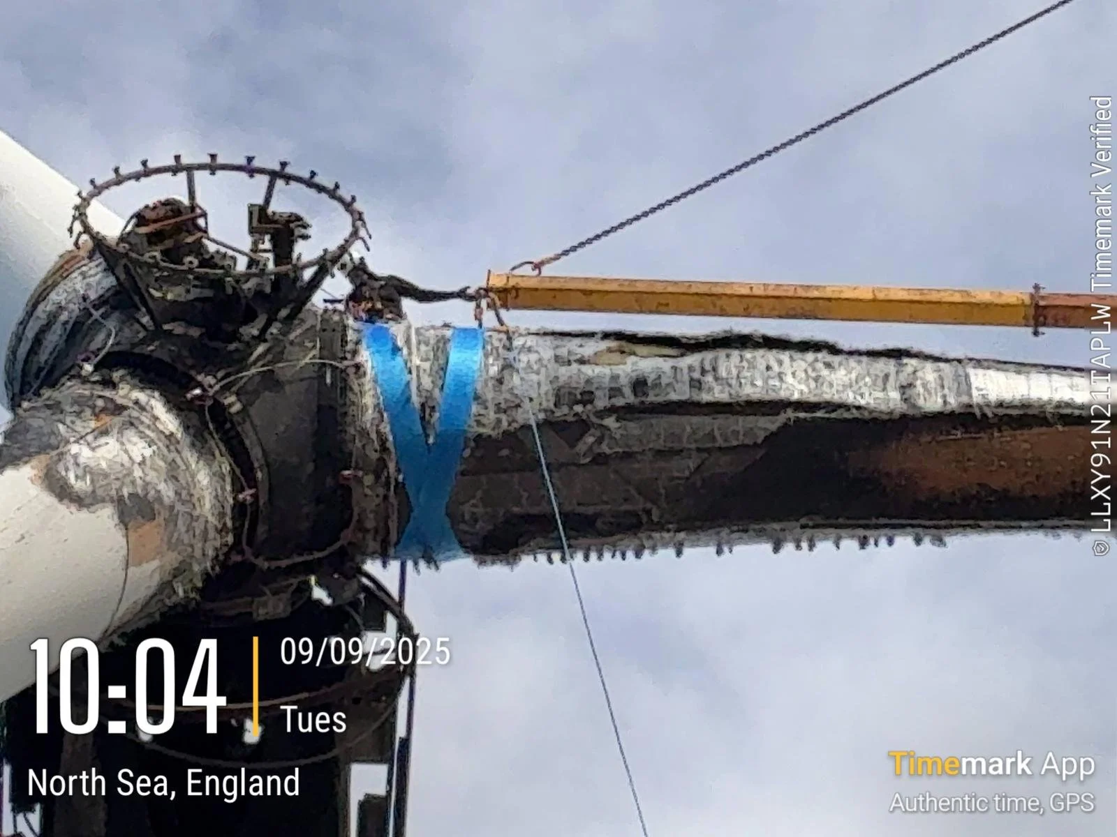 Close-up of a damaged telephone or utility pole with wires and equipment, near the North Sea coast in England, under a cloudy sky.