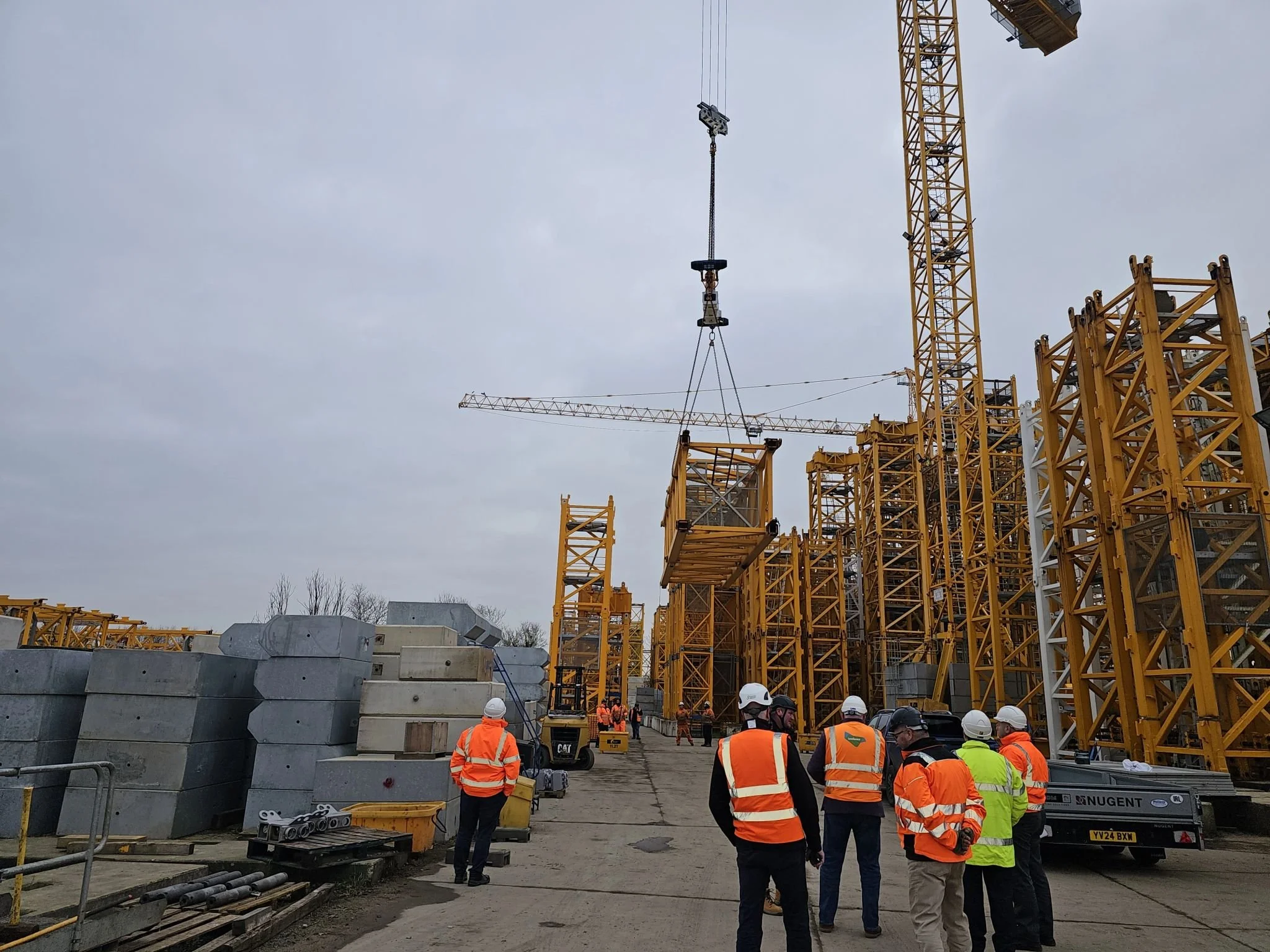 Construction site with multiple yellow cranes and construction workers wearing safety vests and helmets.