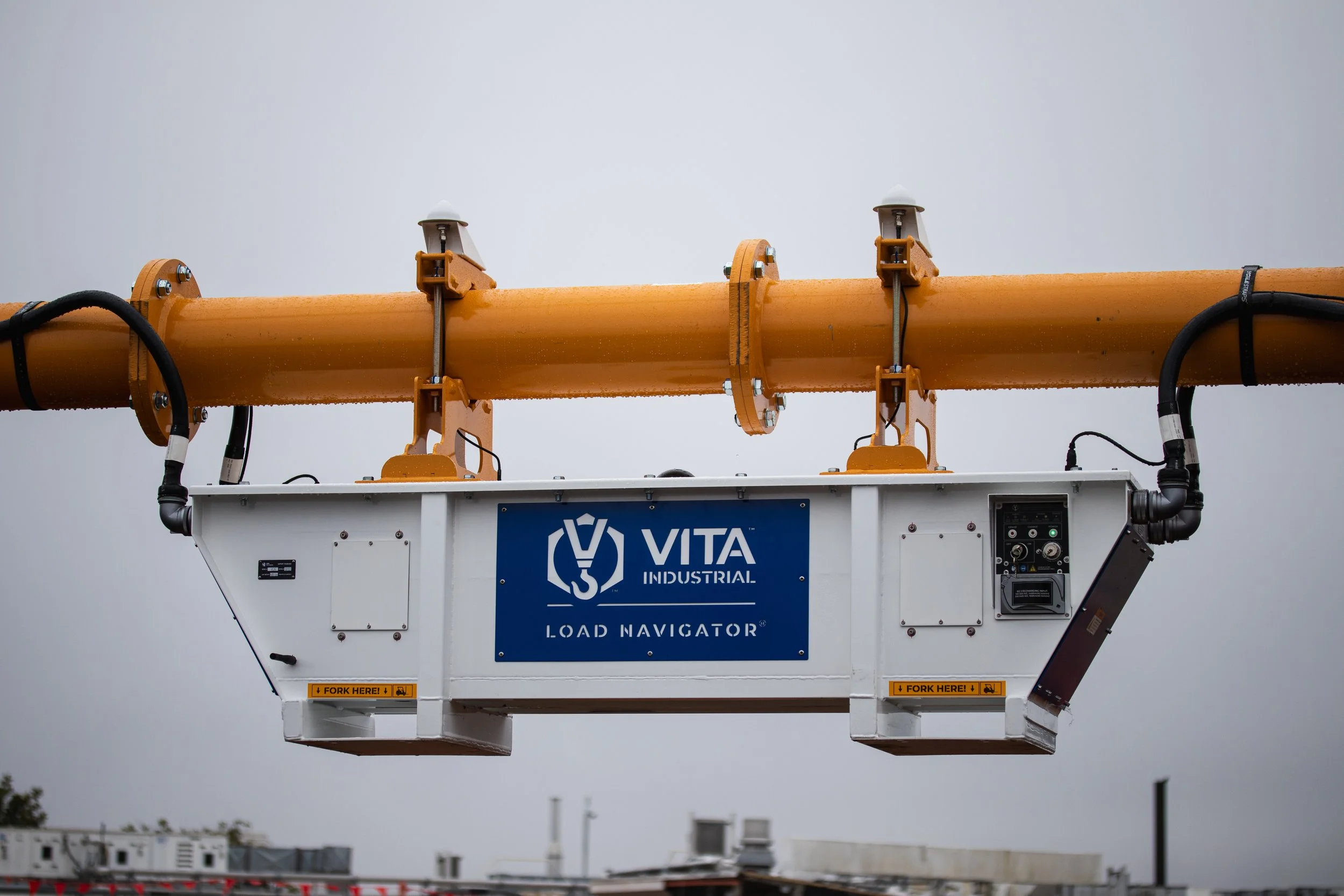 Construction crane lift with orange boom and white load navigator platform on a cloudy day.