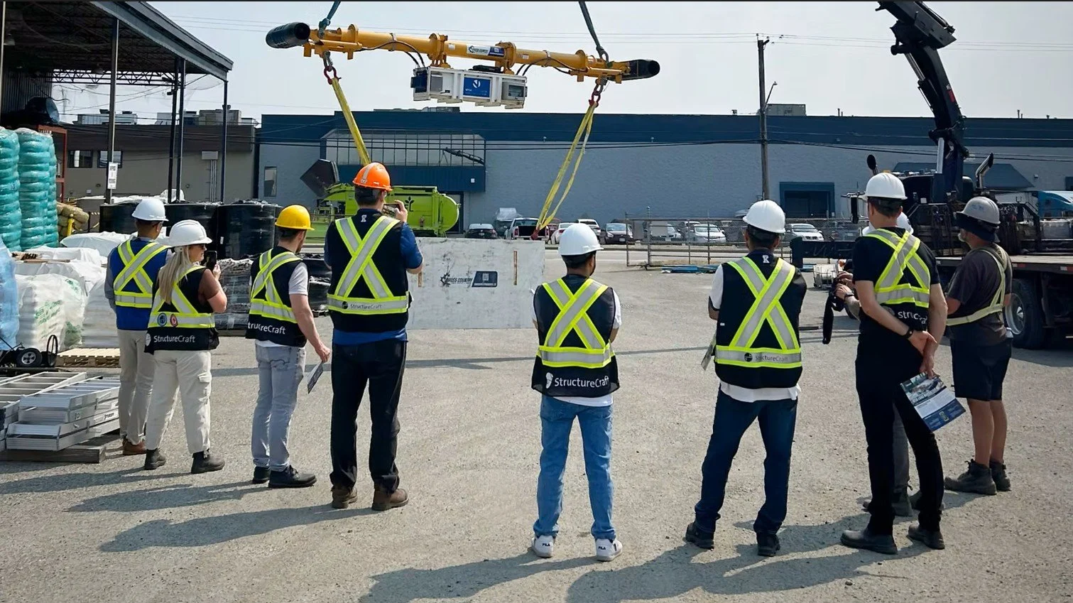 Group of construction workers and engineers wearing safety vests and helmets observing a large construction site with a crane lifting equipment