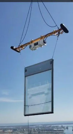 A large glass window panel suspended in the air by a crane with cables during a construction or installation process.