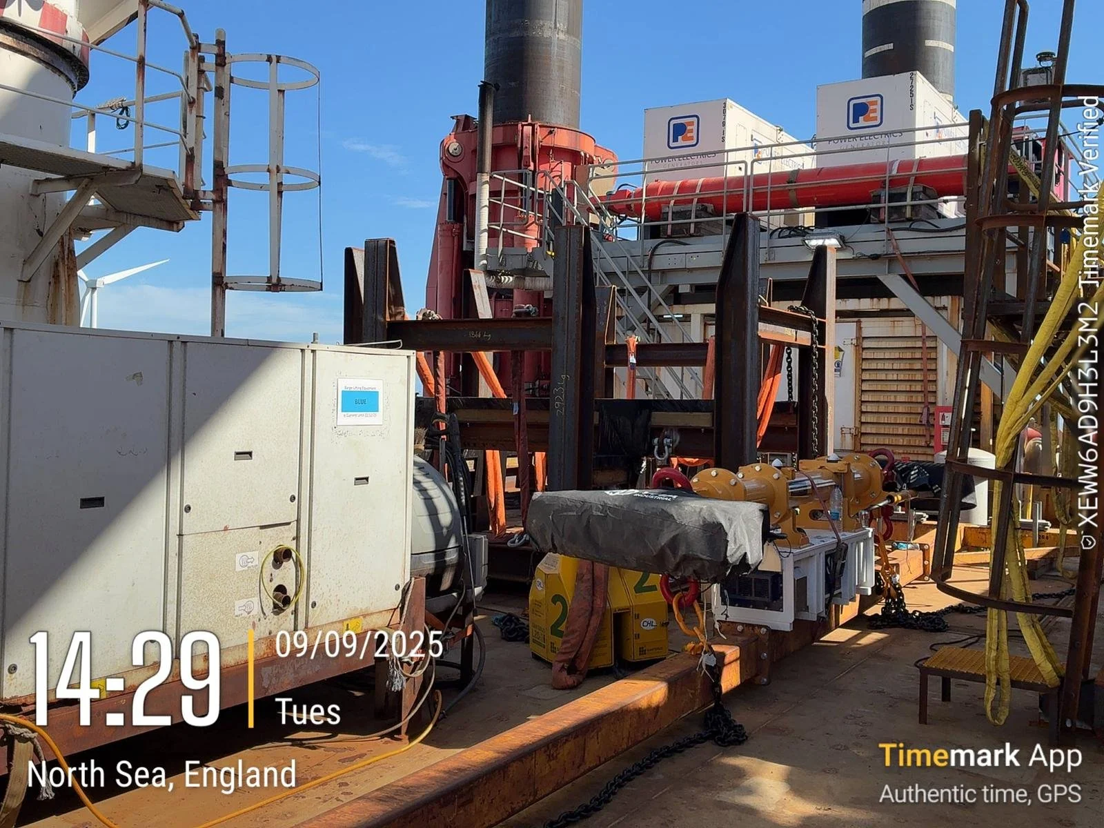 Close-up view of offshore oil rig equipment and machinery, including pipes, containers, and structural components, with a clear blue sky in the background.