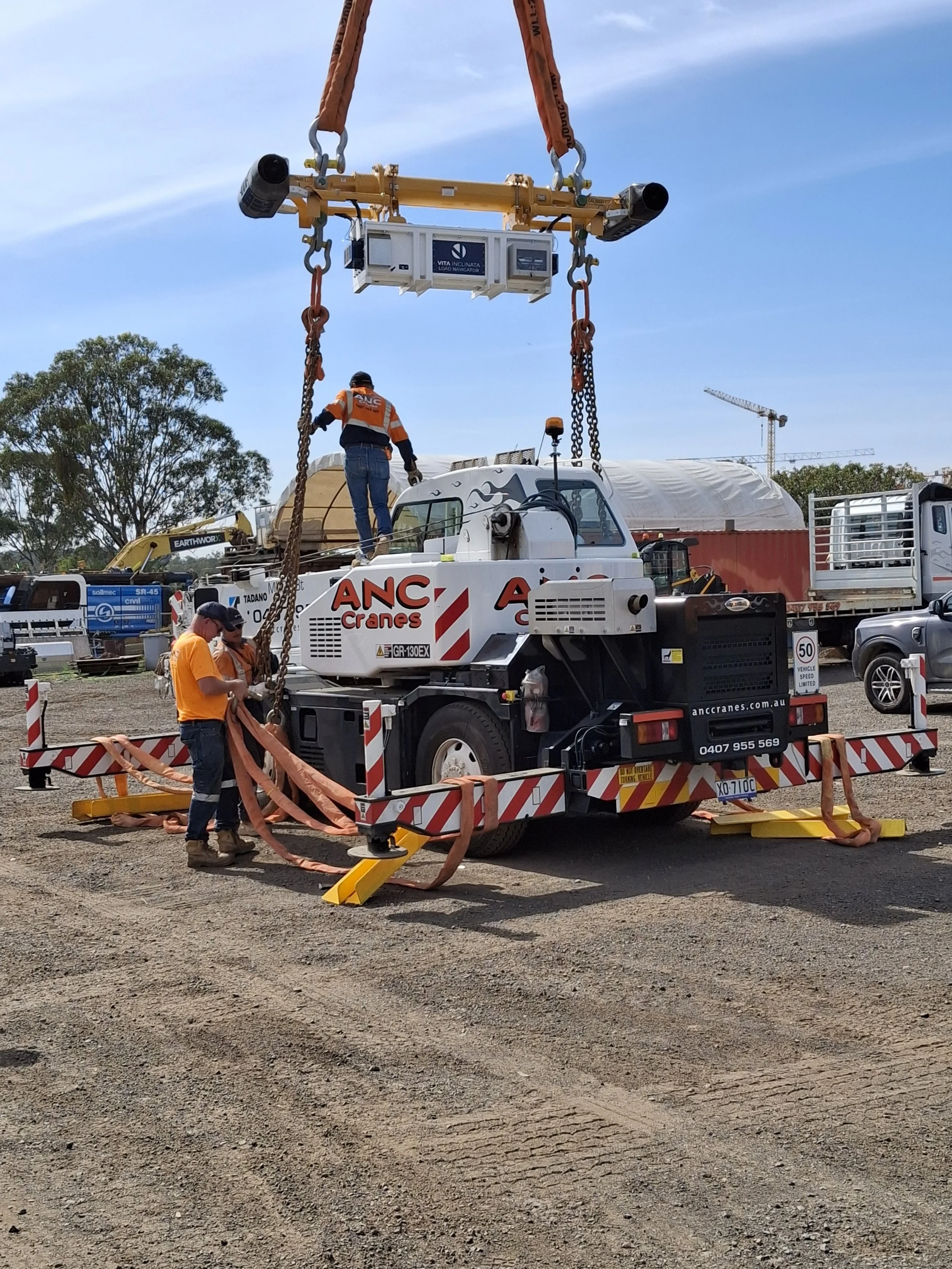 Workers operating a crane on a truck to lift and secure equipment at a construction site.
