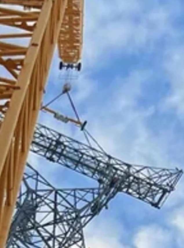 A tower crane is building a structure, with a partly assembled wooden framework, against a blue sky with some clouds.