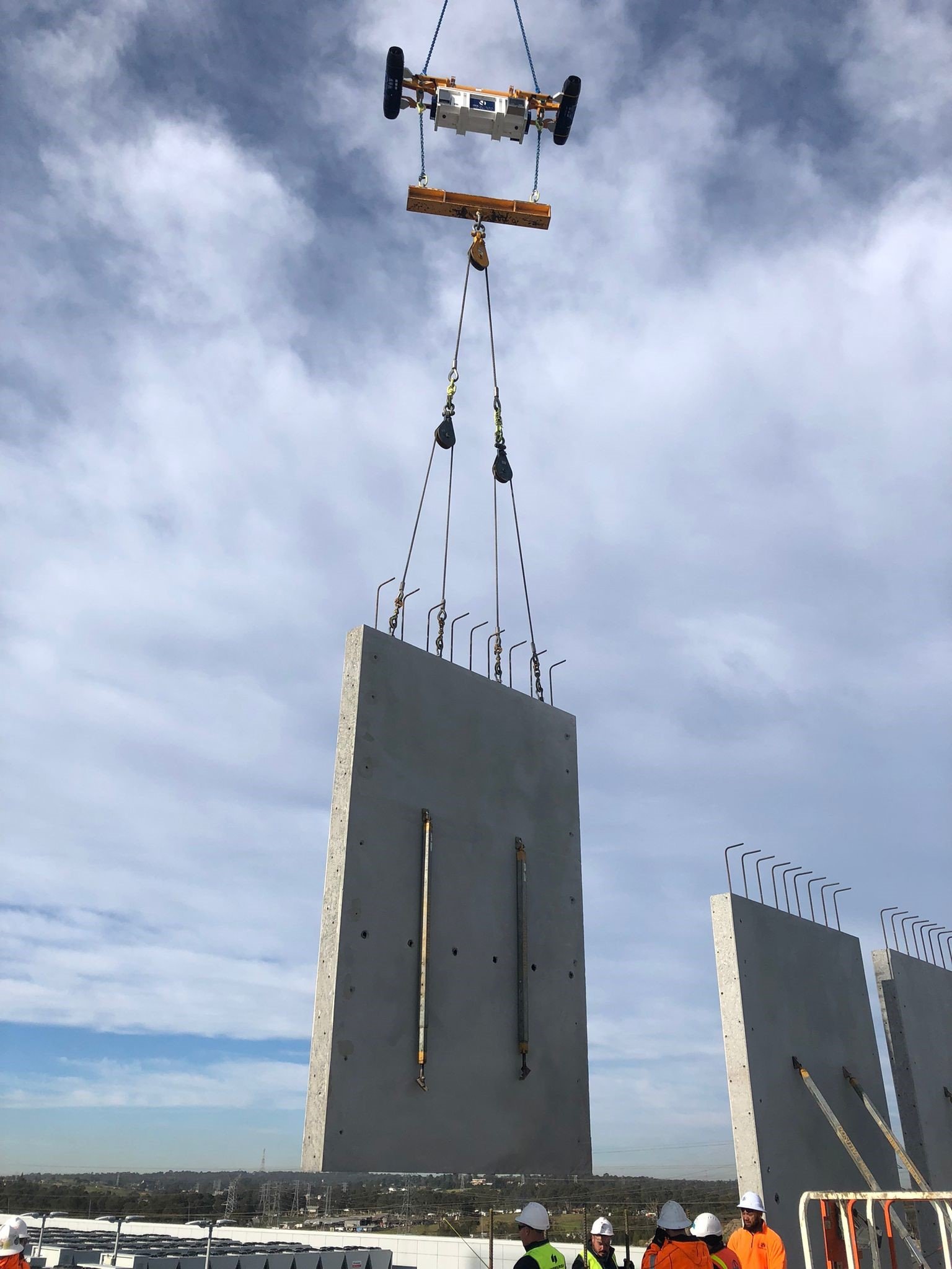 Construction workers at a high-rise building site supervising the installation of large concrete wall panels using a crane.