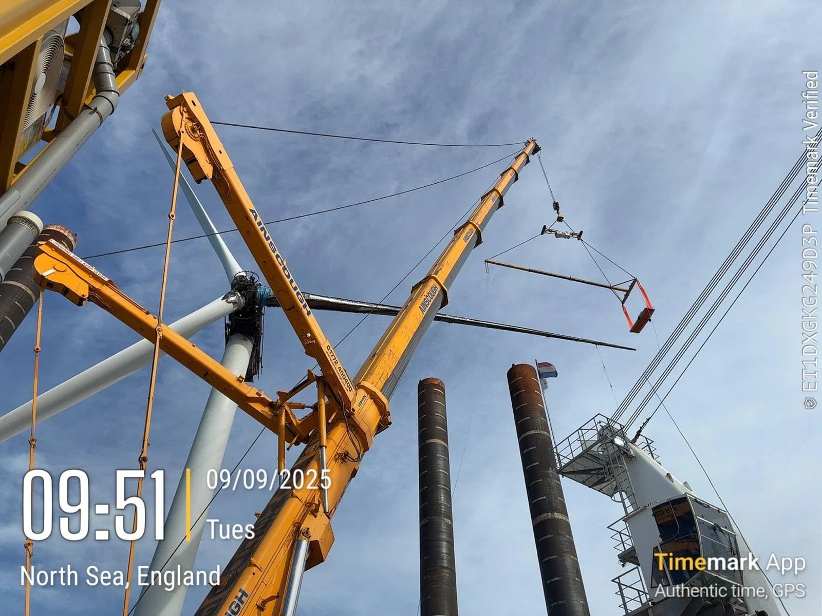 Construction scene with a large yellow crane lifting equipment against a sky with some clouds, at North Sea, England.