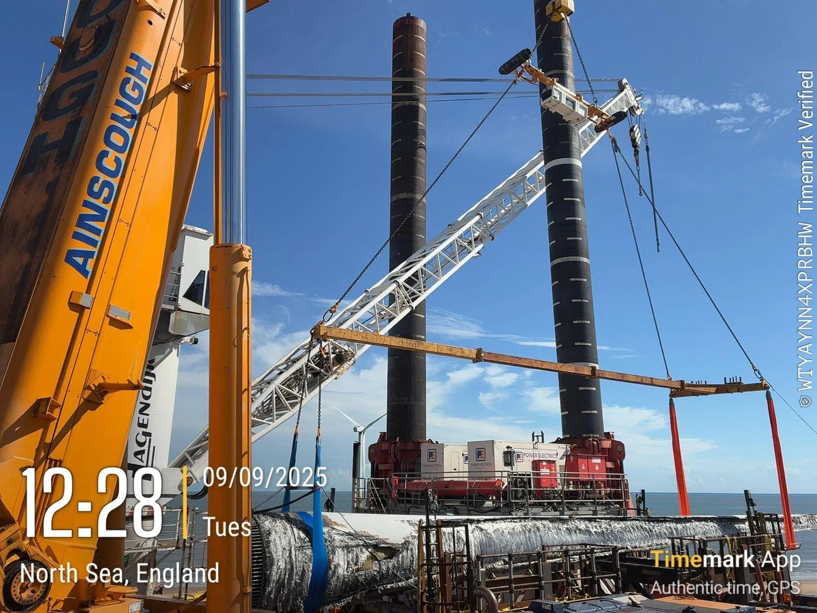 Construction site with large machinery, including cranes and industrial equipment, on a platform near the ocean, with a clear blue sky in the background.