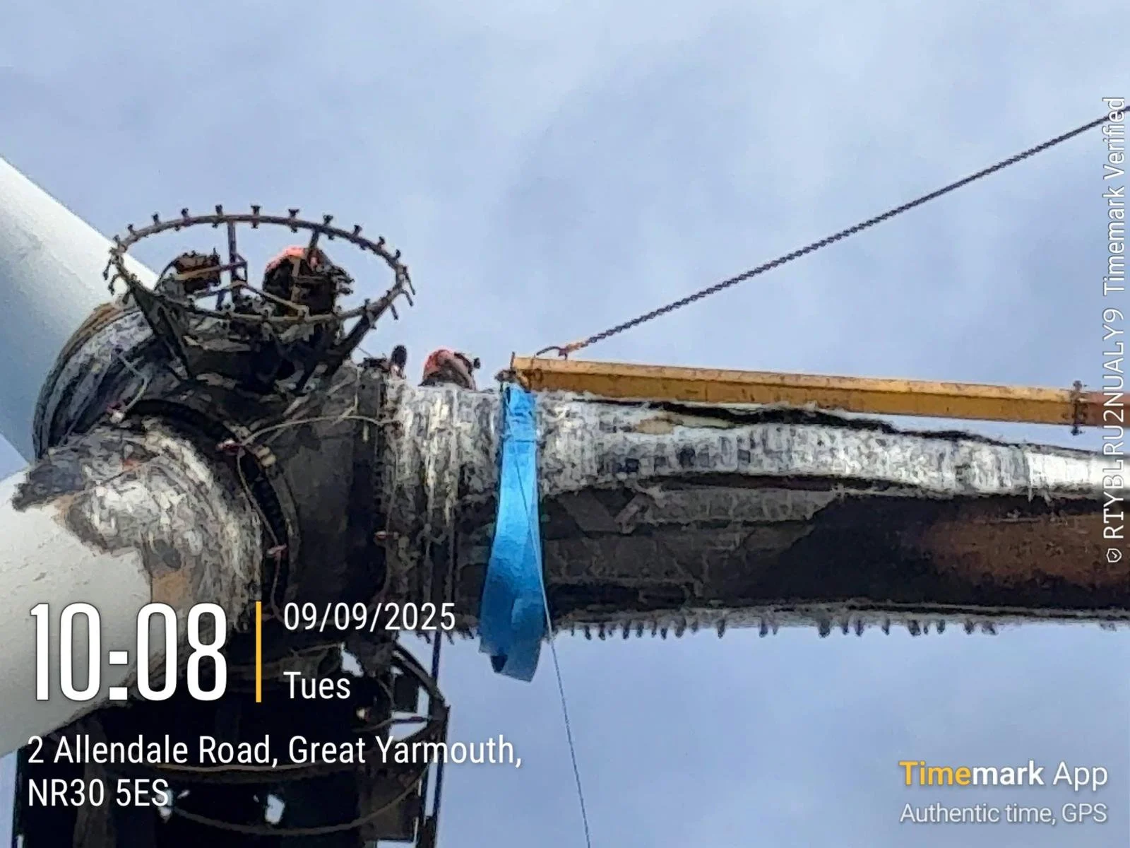 Close-up of a utility or communication pole under maintenance, with workers at the top and construction equipment, against a blue sky.