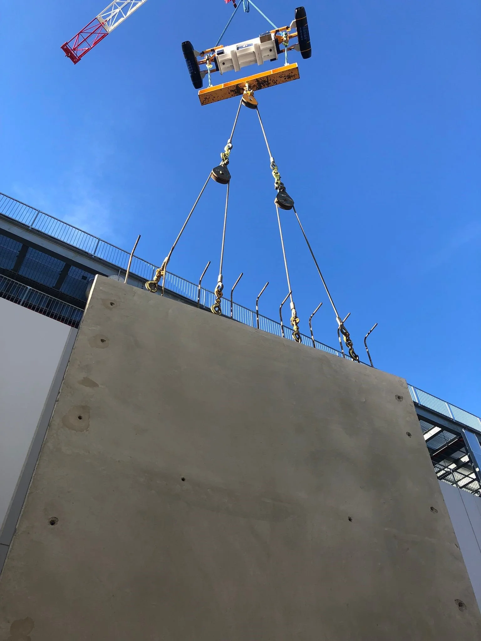 A construction crane lifting a large concrete panel into place at a construction site.