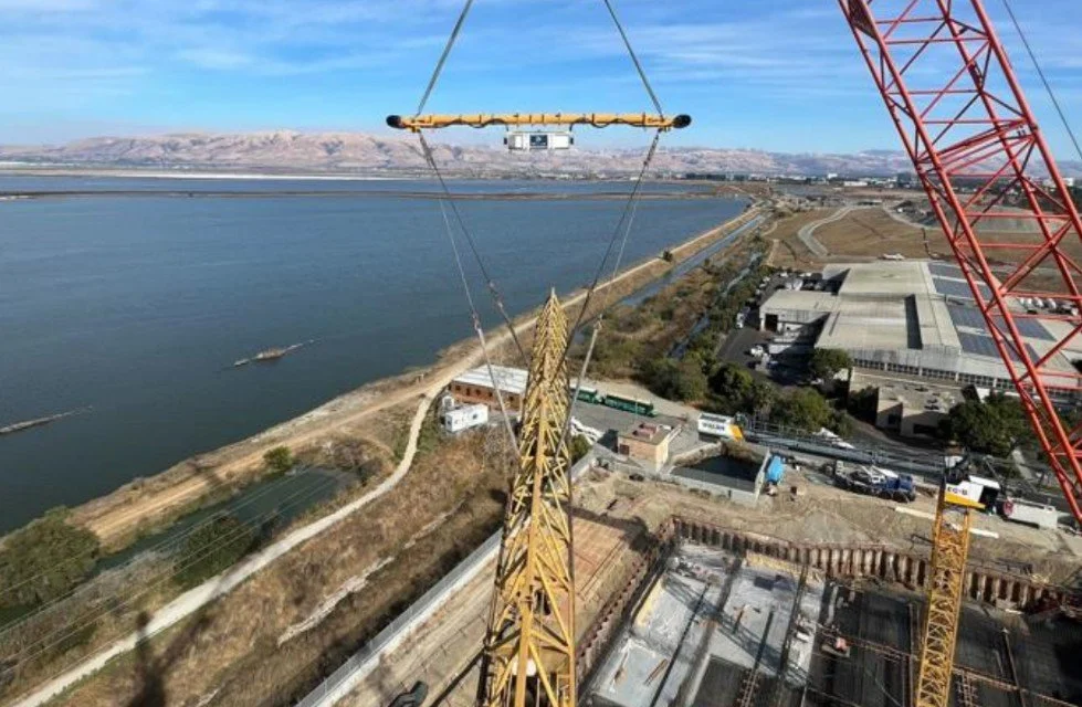 Construction site with a large yellow crane and a view of a river and mountains in the background