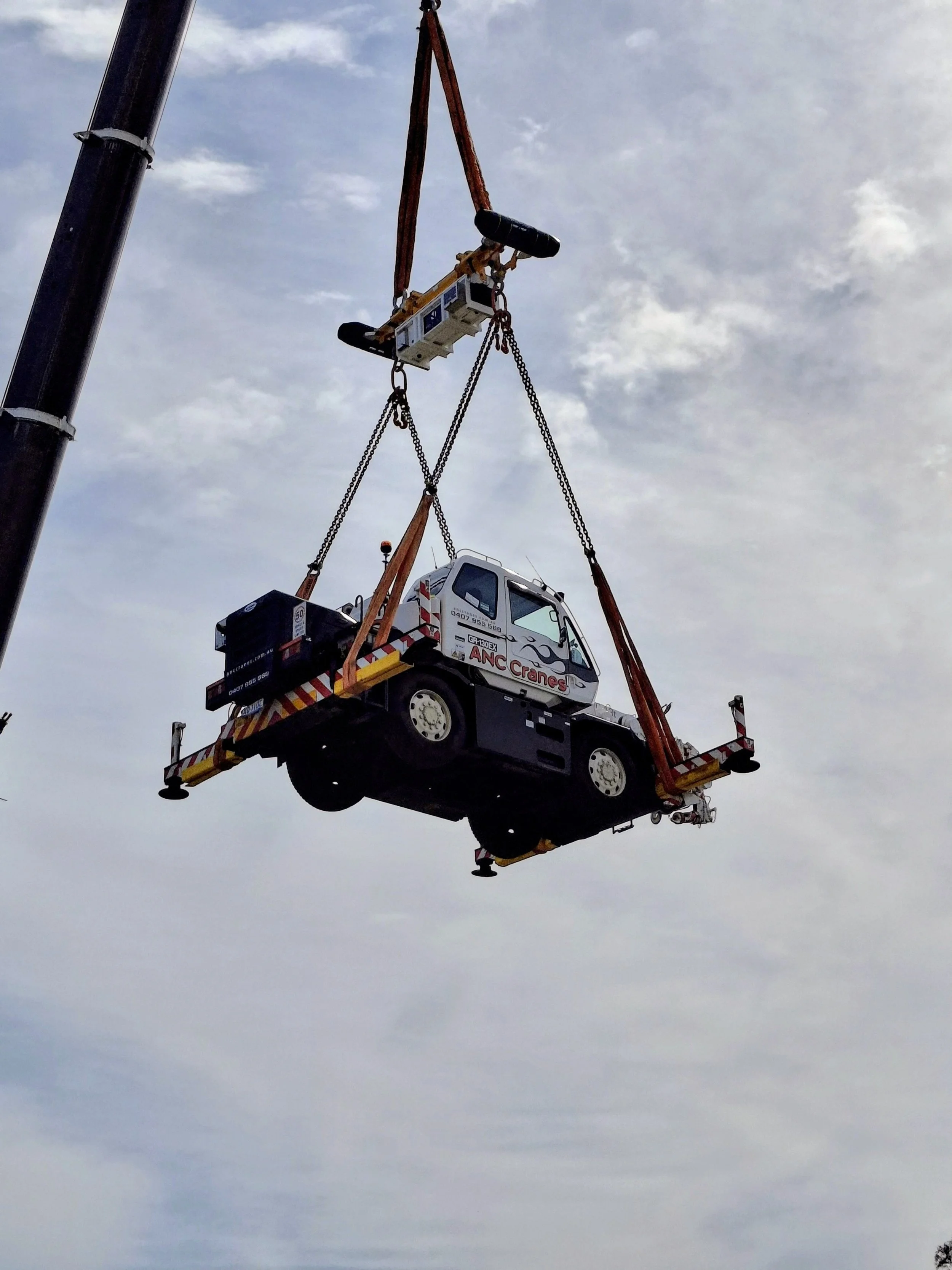 A crane lifting a small truck with the company logo 'ANC Cranes' visible on the side.