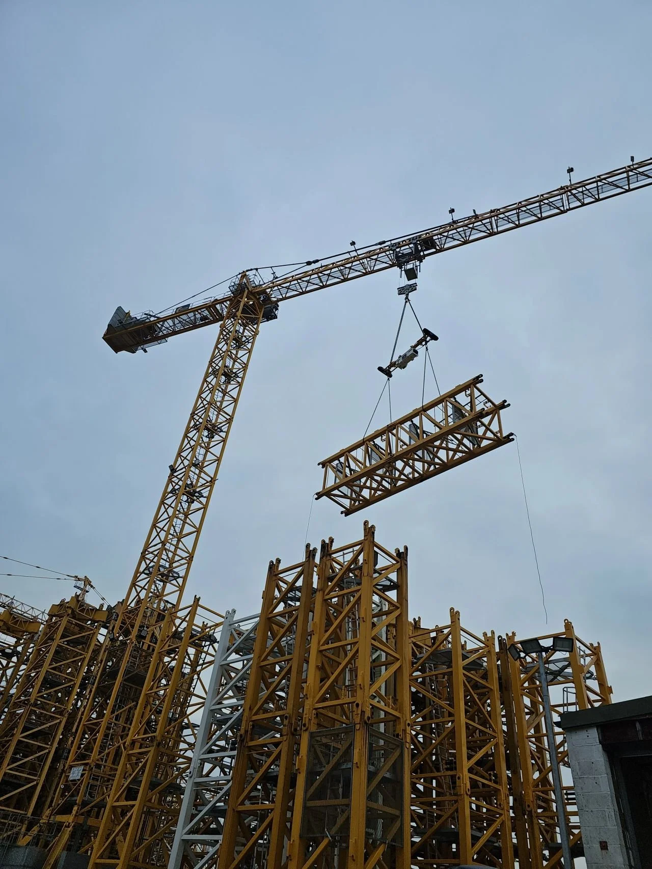 Construction site with a tall crane lifting yellow steel structures into place against a cloudy sky.