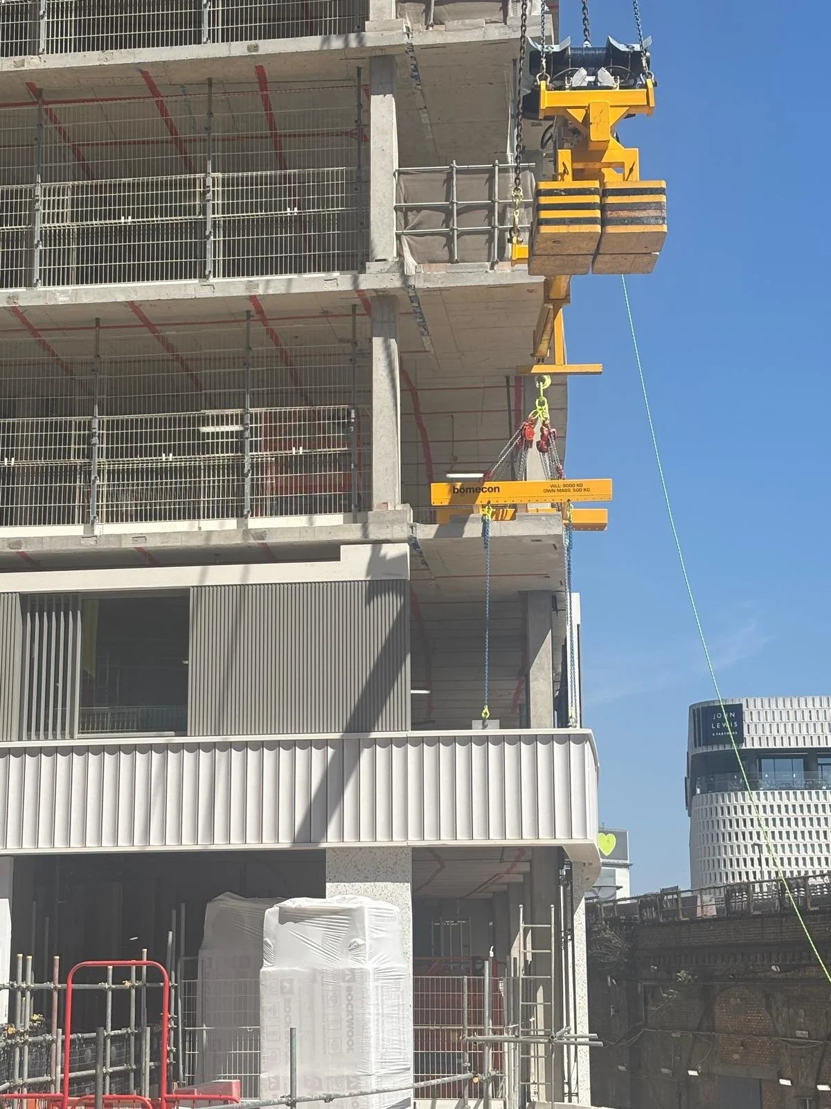 Construction site with a multi-story building under construction. Yellow crane equipment visible, with safety barriers and building materials.