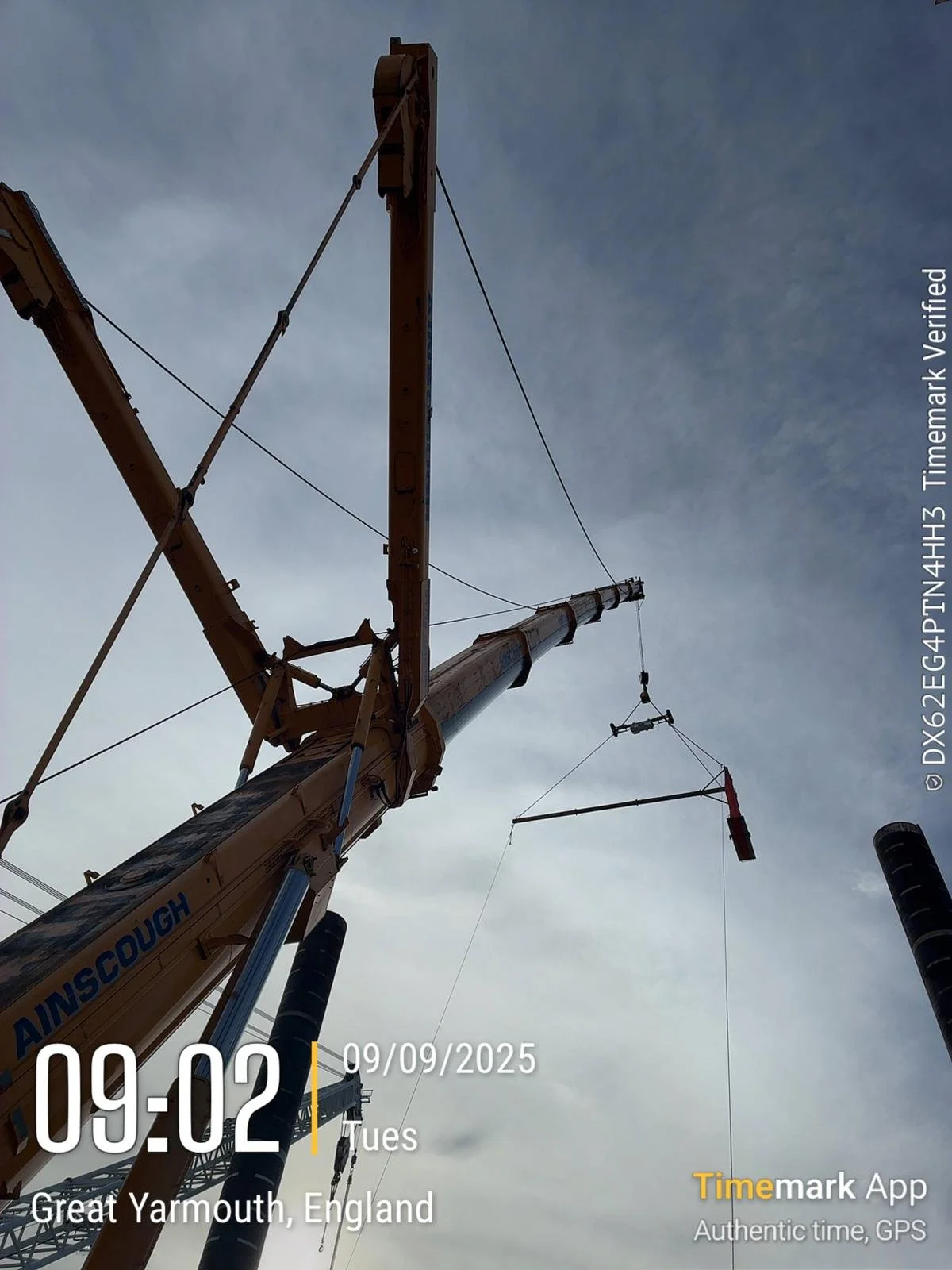 Close-up of a construction crane arm with a wind vane attached, set against a cloudy sky in Great Yarmouth, England.