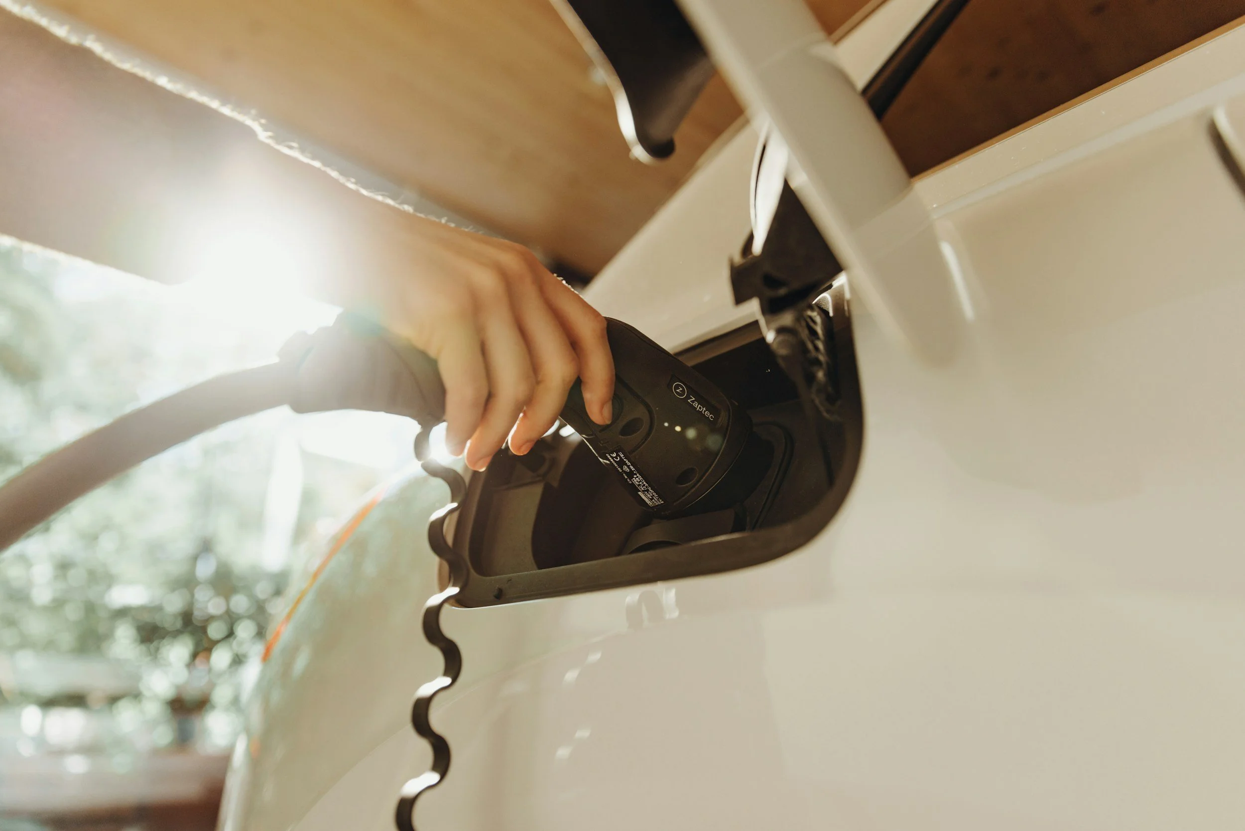 Close-up of a person charging an electric vehicle with a Zaptec charging station, with sunlight shining in the background.