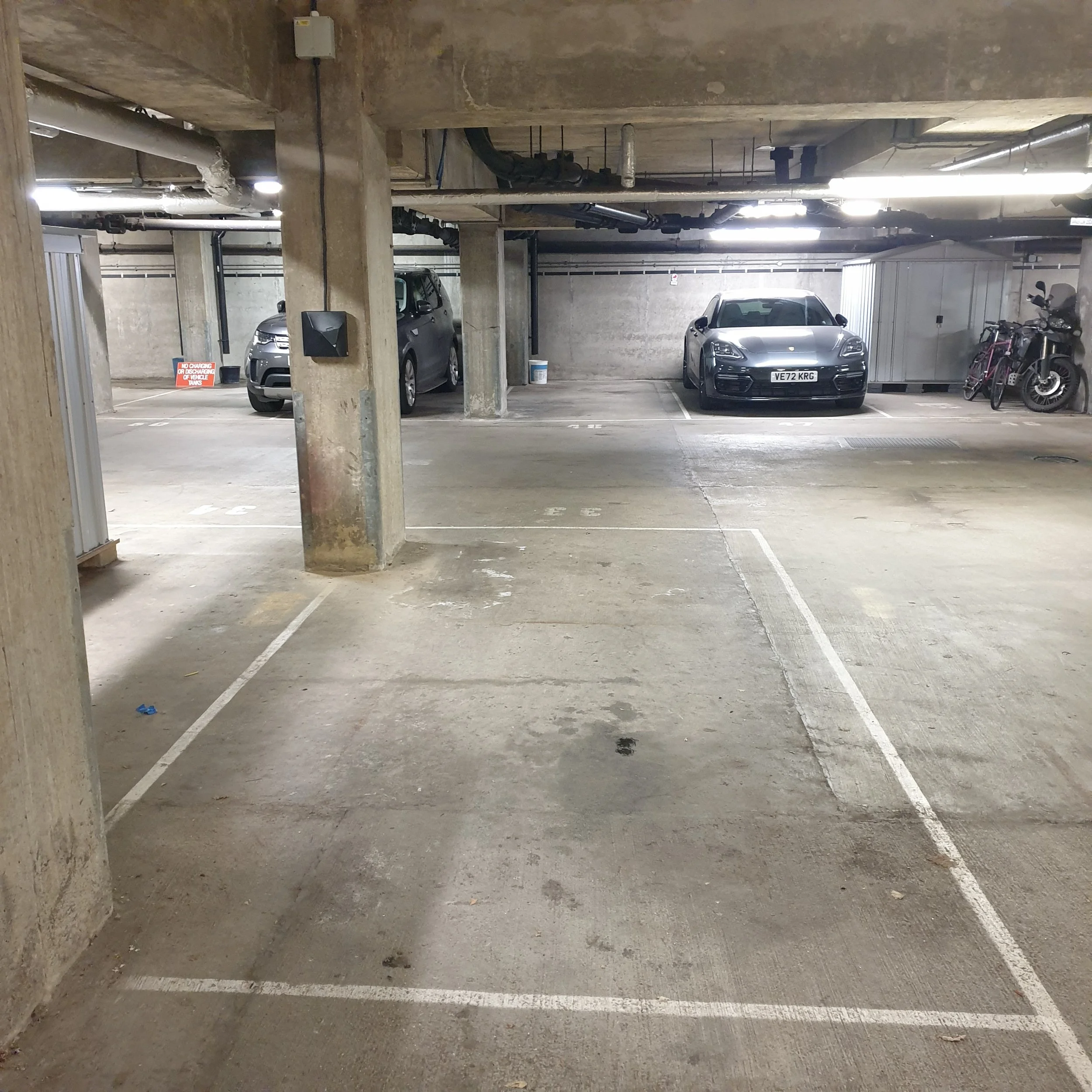 Underground parking garage with three parked cars, bicycles, and a storage shed in the background.