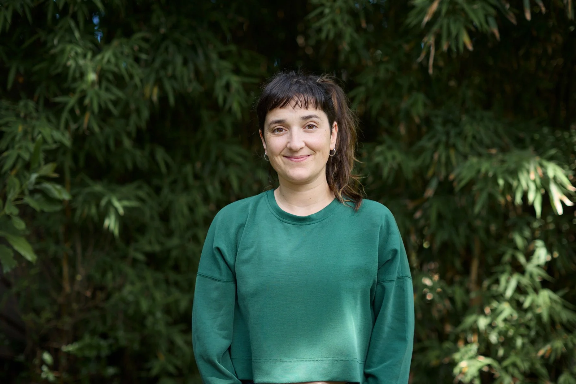 Mujer con camiseta verde claro frente a fondo de arbustos verdes.