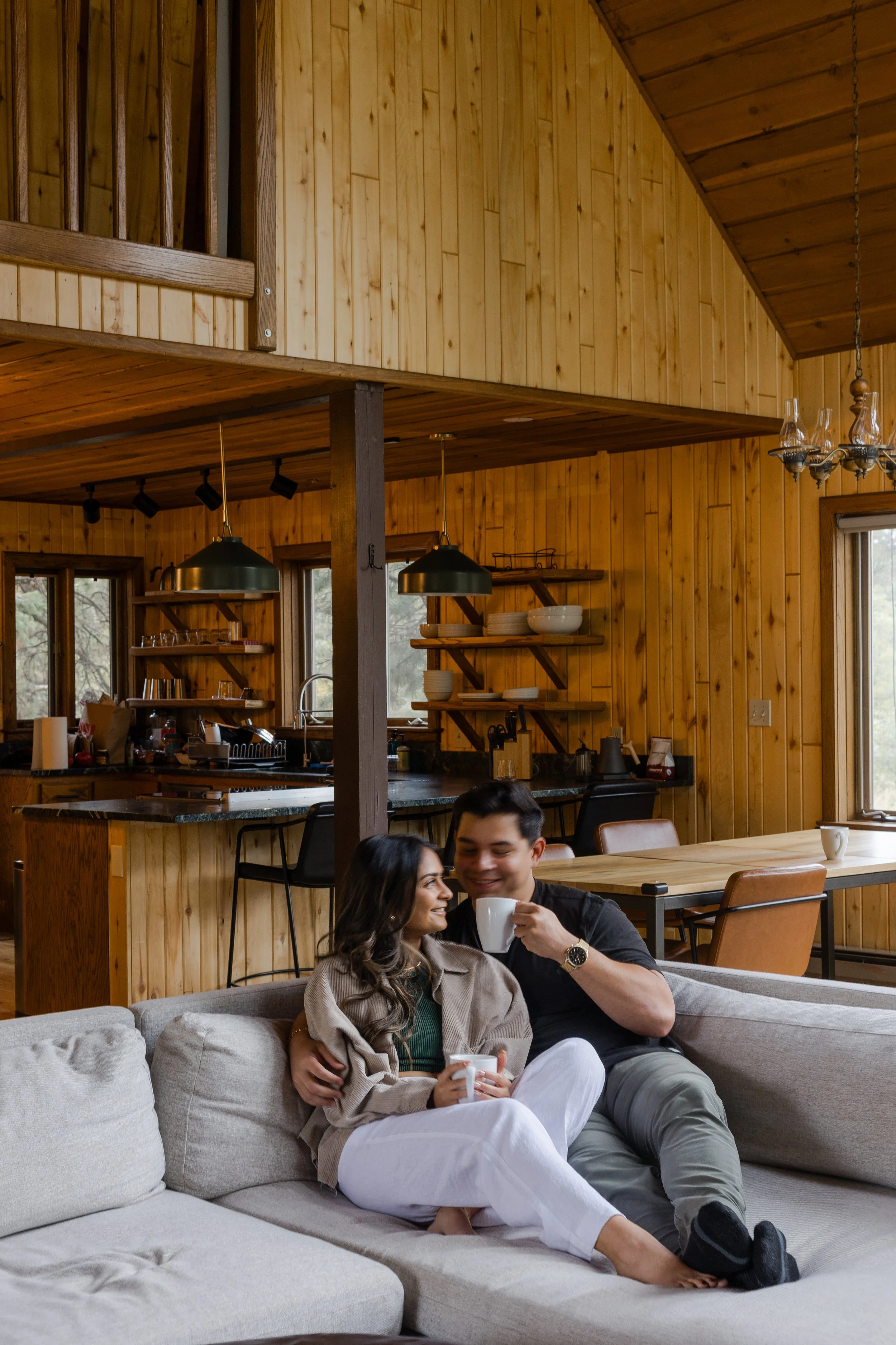 Couple snuggling on the couch with their coffee mugs in their Airbnb on the morning of their elopement. Photography by Trail Magic Elopements and Micro Weddings.