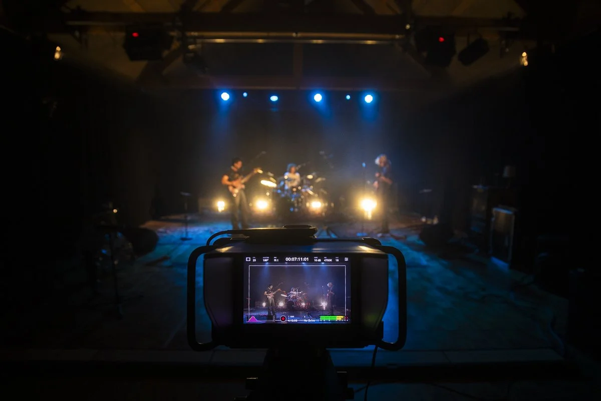 A stage with a band performing under blue spotlights, filmed from a camera displaying the scene on its screen.