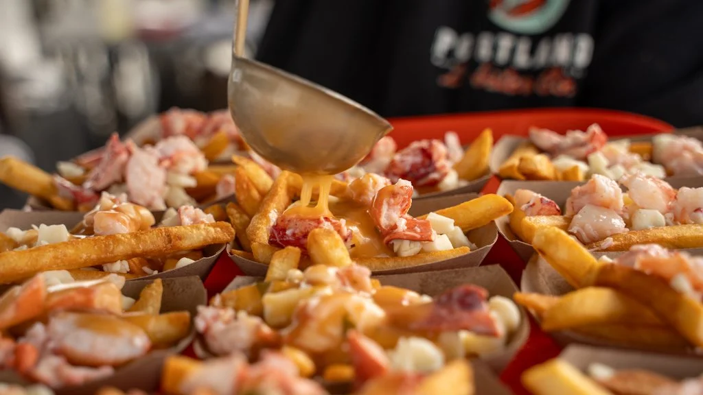 Close-up of loaded fries topped with shrimp, crab meat, cheese, and sauce on a red tray, with a person in the background.